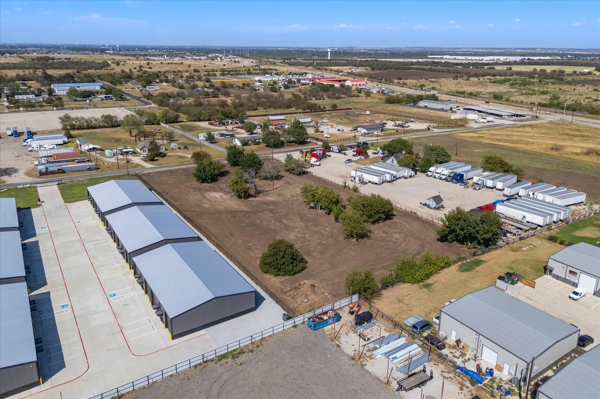 Multiple metal storage buildings with gray roofs, extensive paved parking, and a fenced perimeter