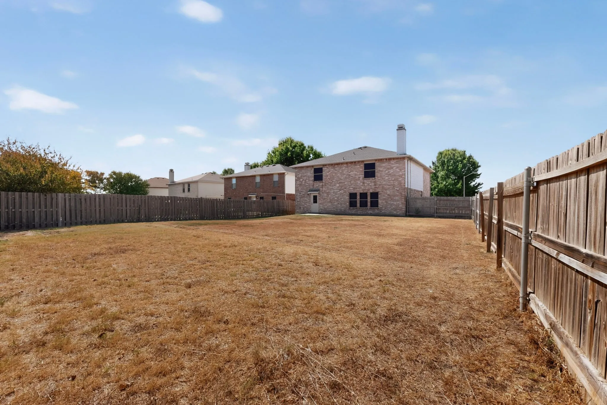 Expansive fenced backyard with a brick exterior and a white chimney