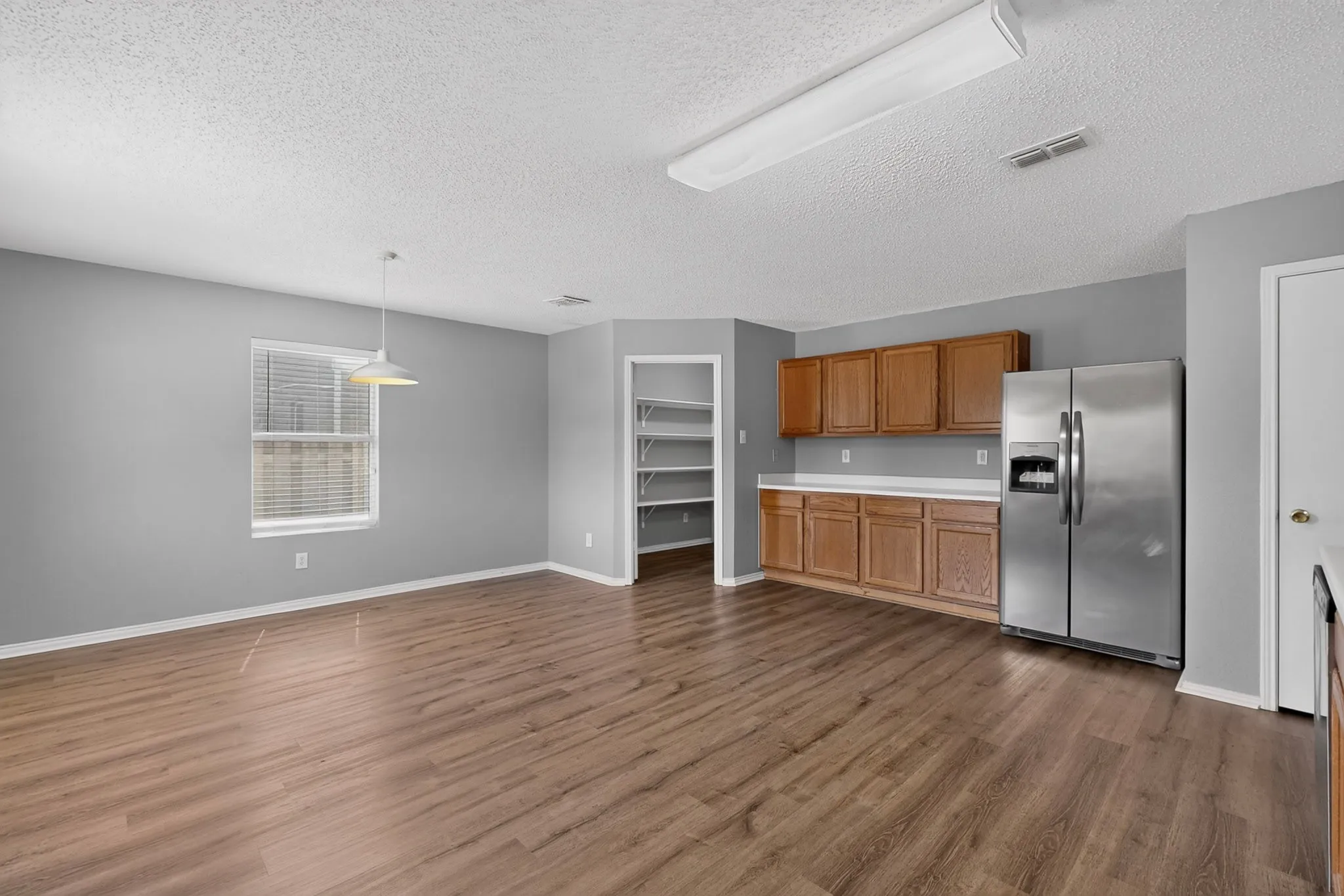 Open-concept living space featuring wood-finish flooring, a window with blinds, recessed shelving, upper and lower cabinetry, and a side-by-side refrigerator