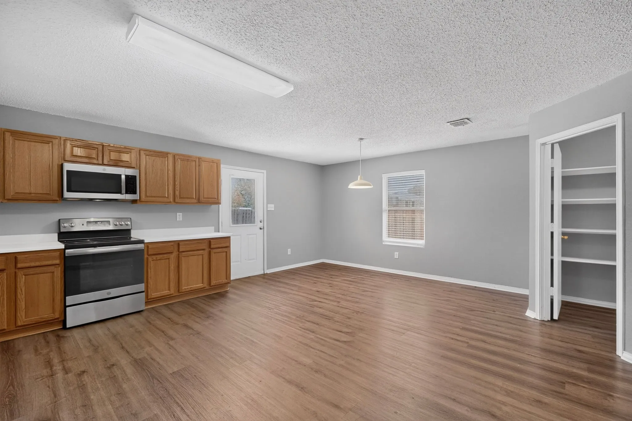 Open-concept living space featuring wood-finish flooring, full kitchen cabinetry, and stainless-steel appliances