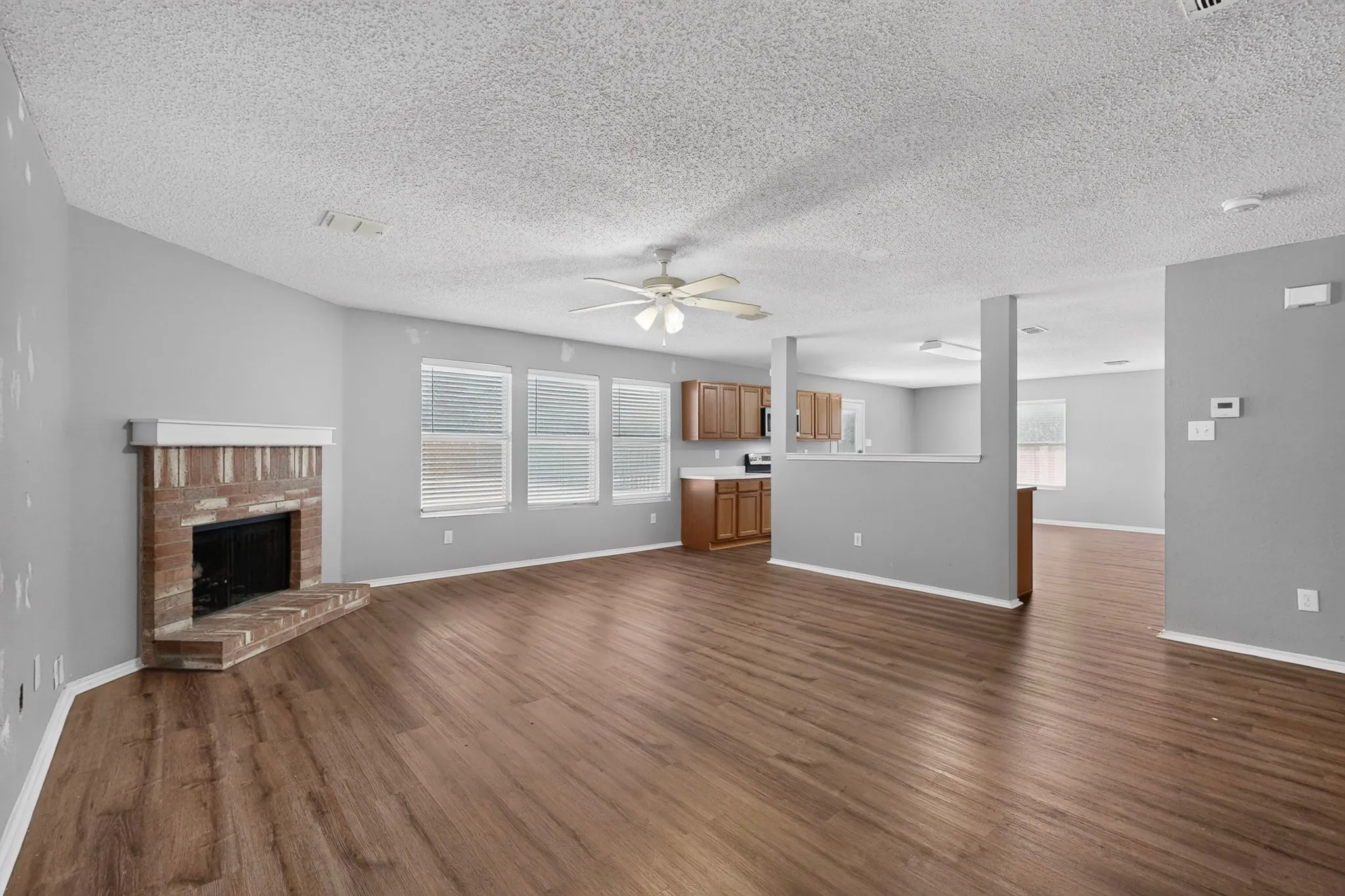 Wood-finish flooring throughout, brick fireplace, multiple windows with blinds, built-in kitchen cabinetry