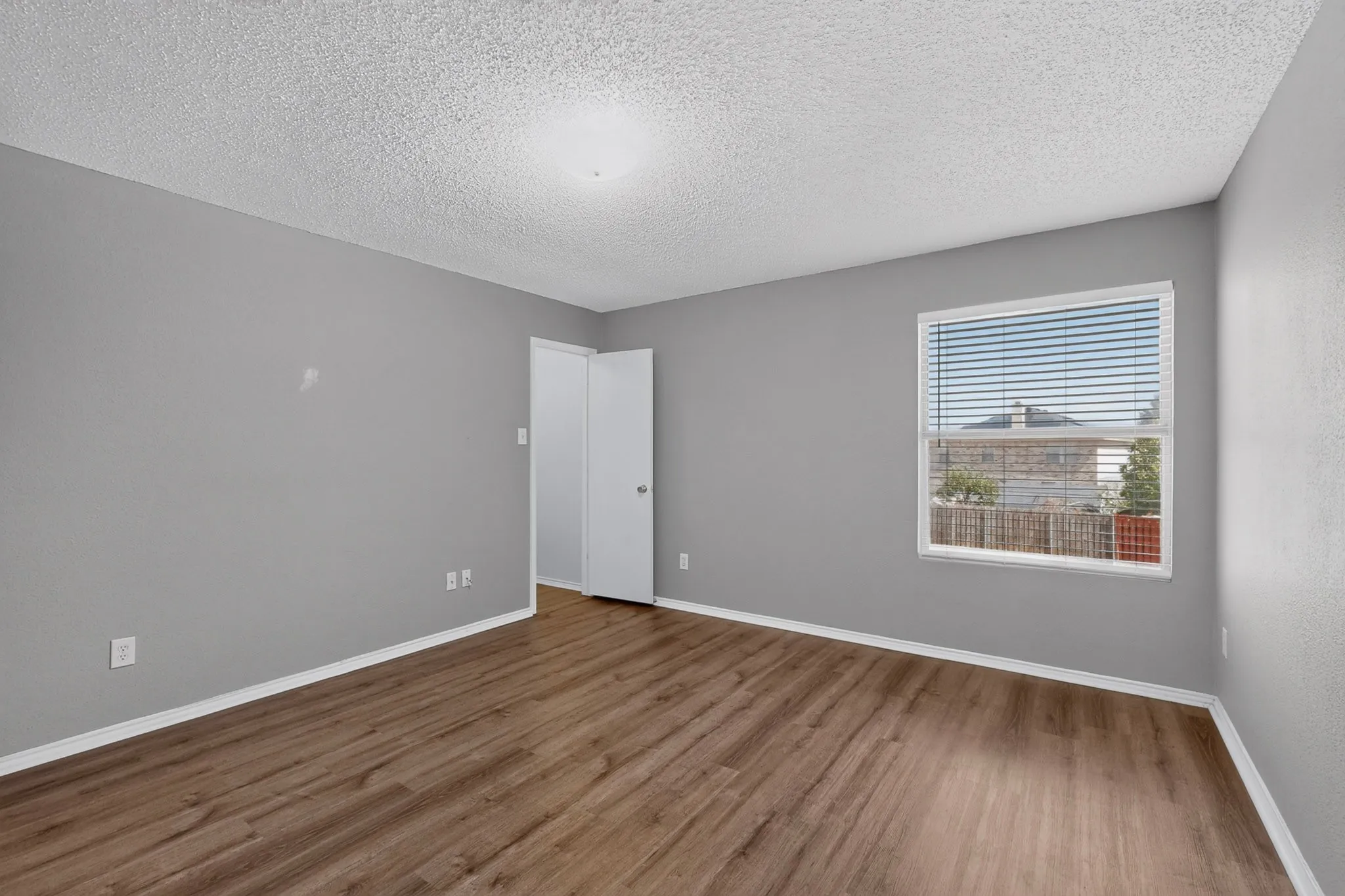 Wood-finish flooring, neutral gray walls, and a single window with horizontal blinds