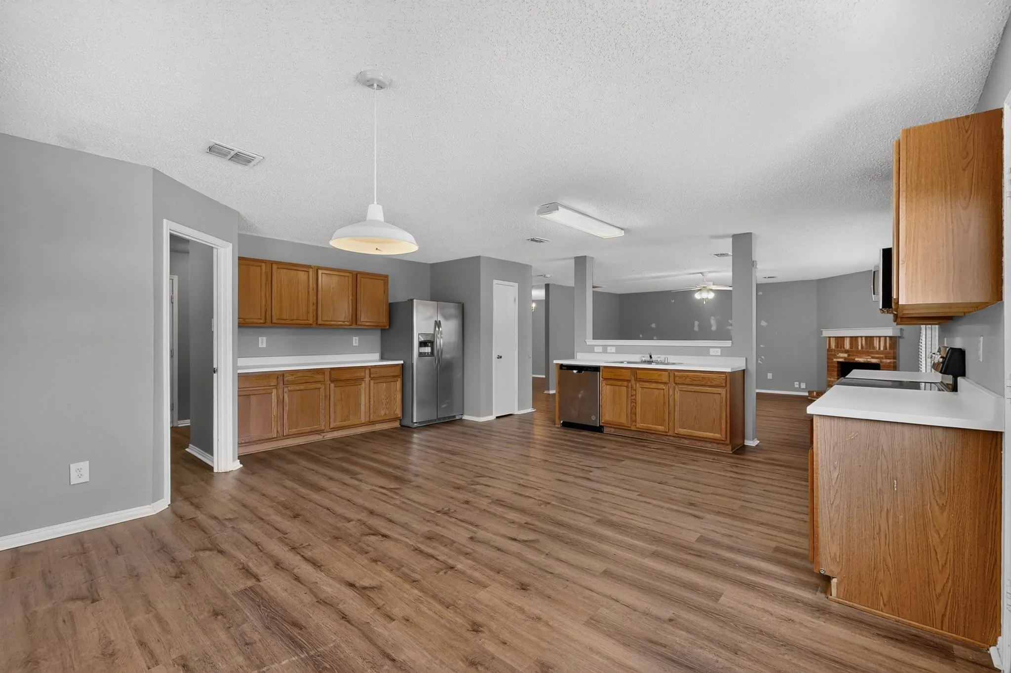Open-concept kitchen with wood-finish flooring, light wood cabinetry, and white countertops