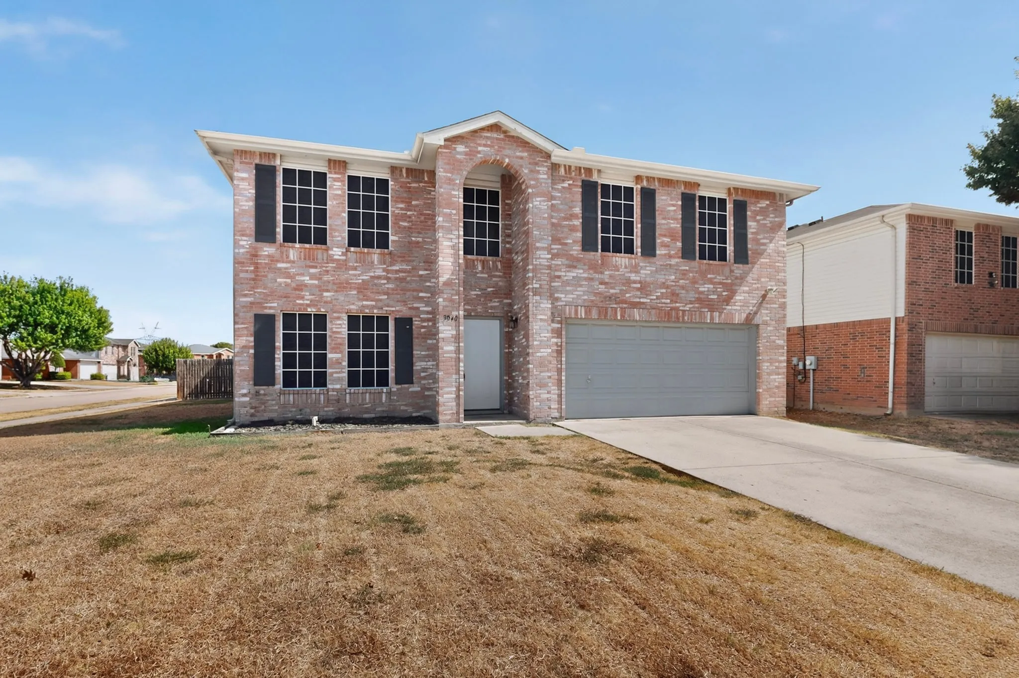 Two-story brick facade with decorative shutters, integrated two-car garage, and concrete driveway