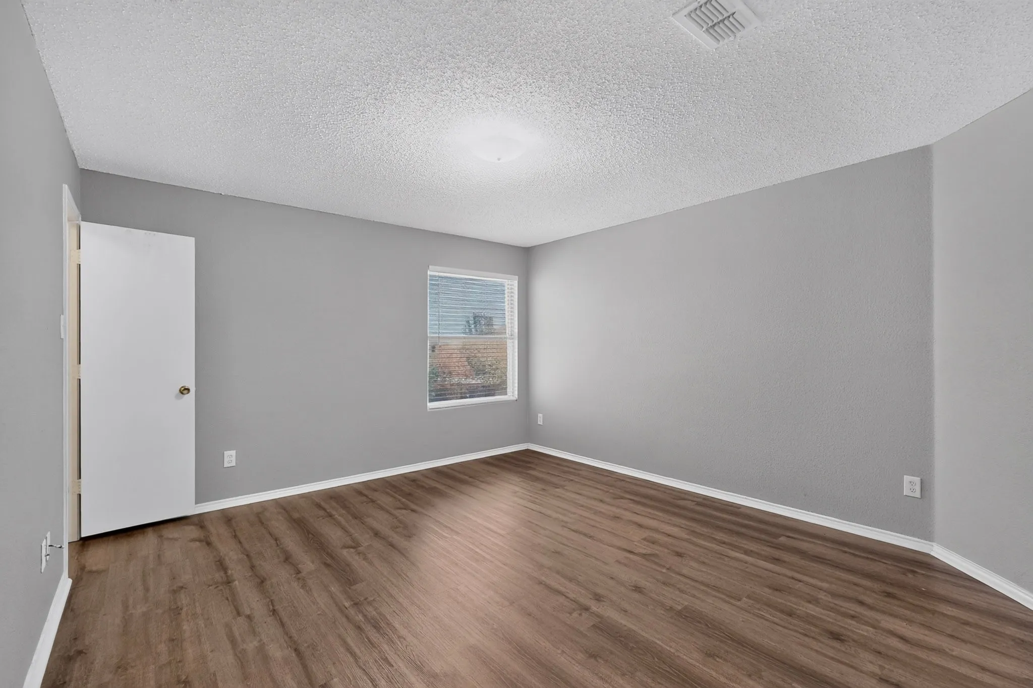 Wood-finish flooring, light gray wall paint, window with blinds, white trim, and a white ceiling