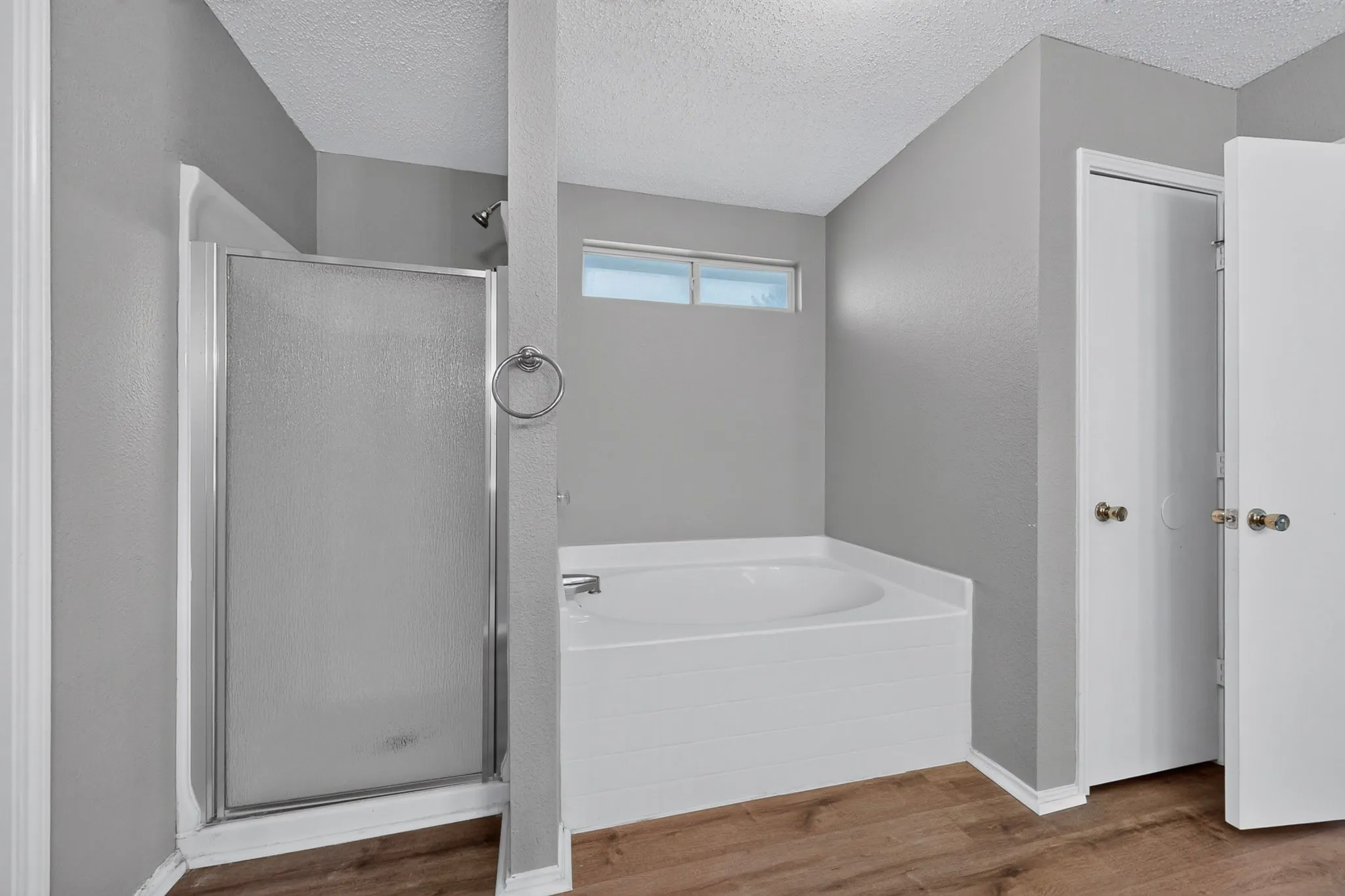 Enclosed shower stall, separate built-in bathtub, high transom window, wood-finish flooring, and white paneled doors