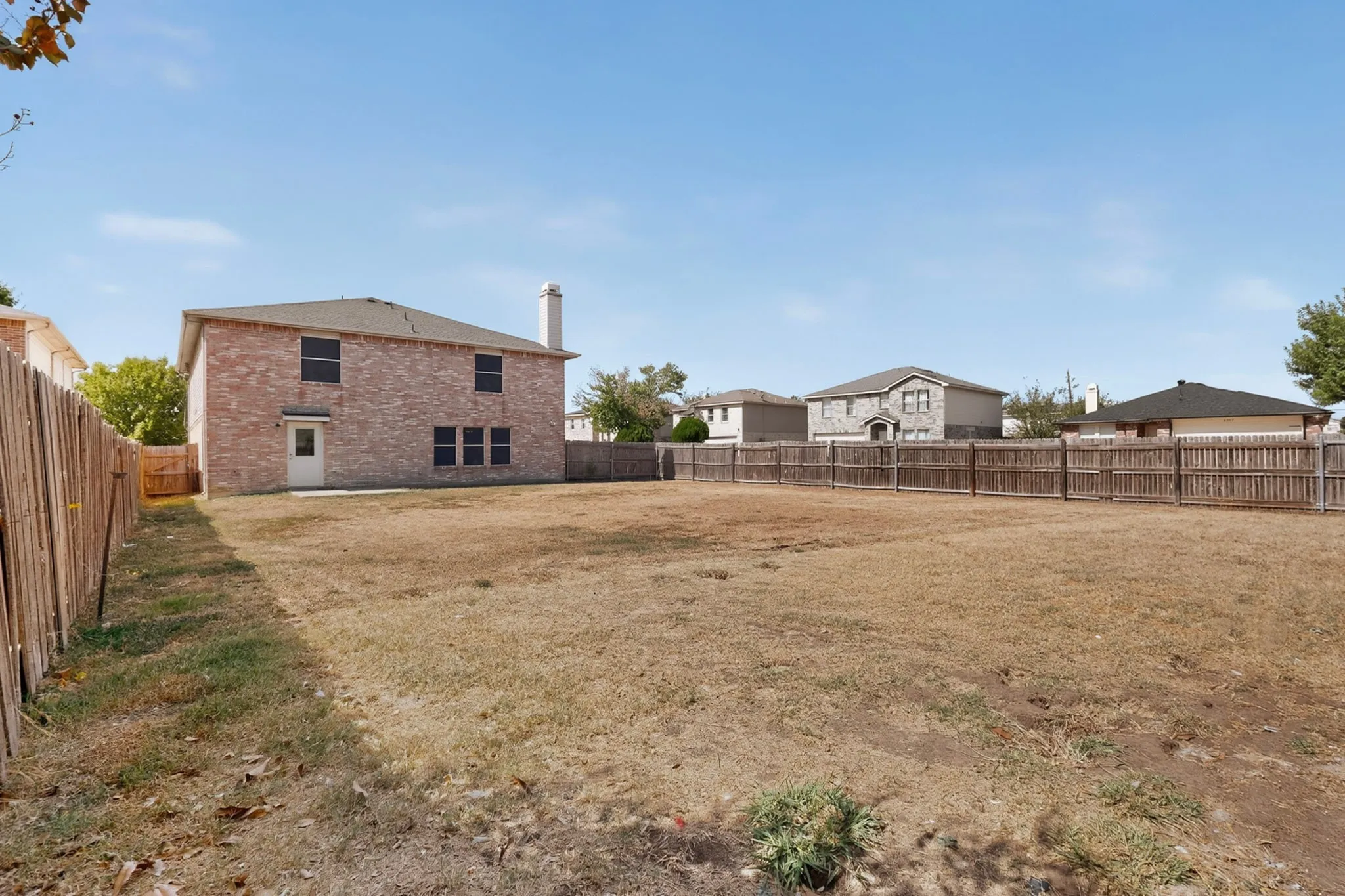 Expansive backyard with a full perimeter wood fence, brick exterior, and a rear patio