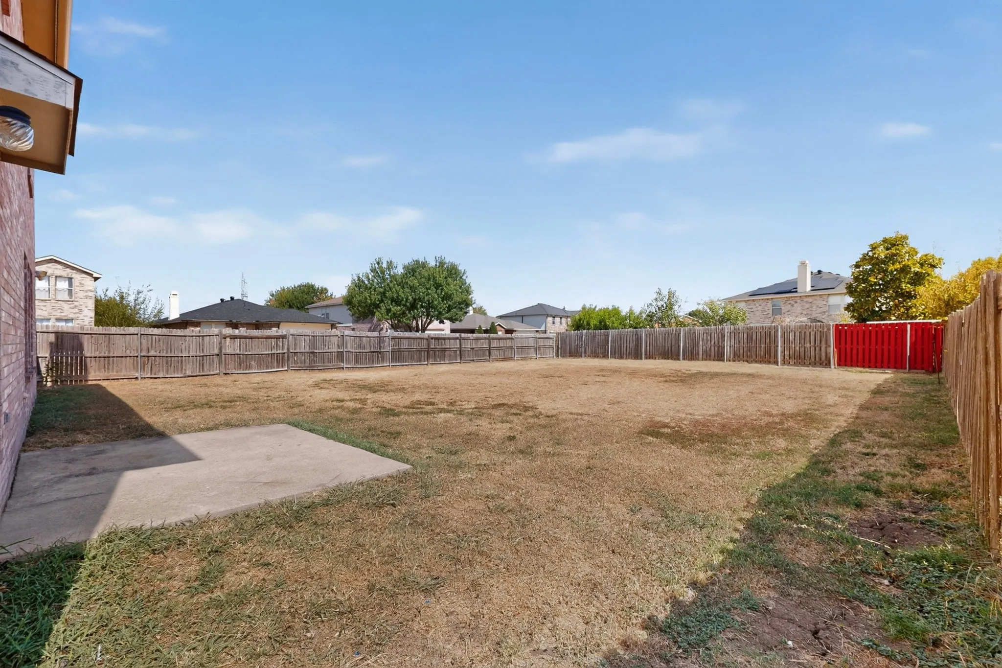 Expansive backyard featuring a concrete patio, wood privacy fencing, and mature trees