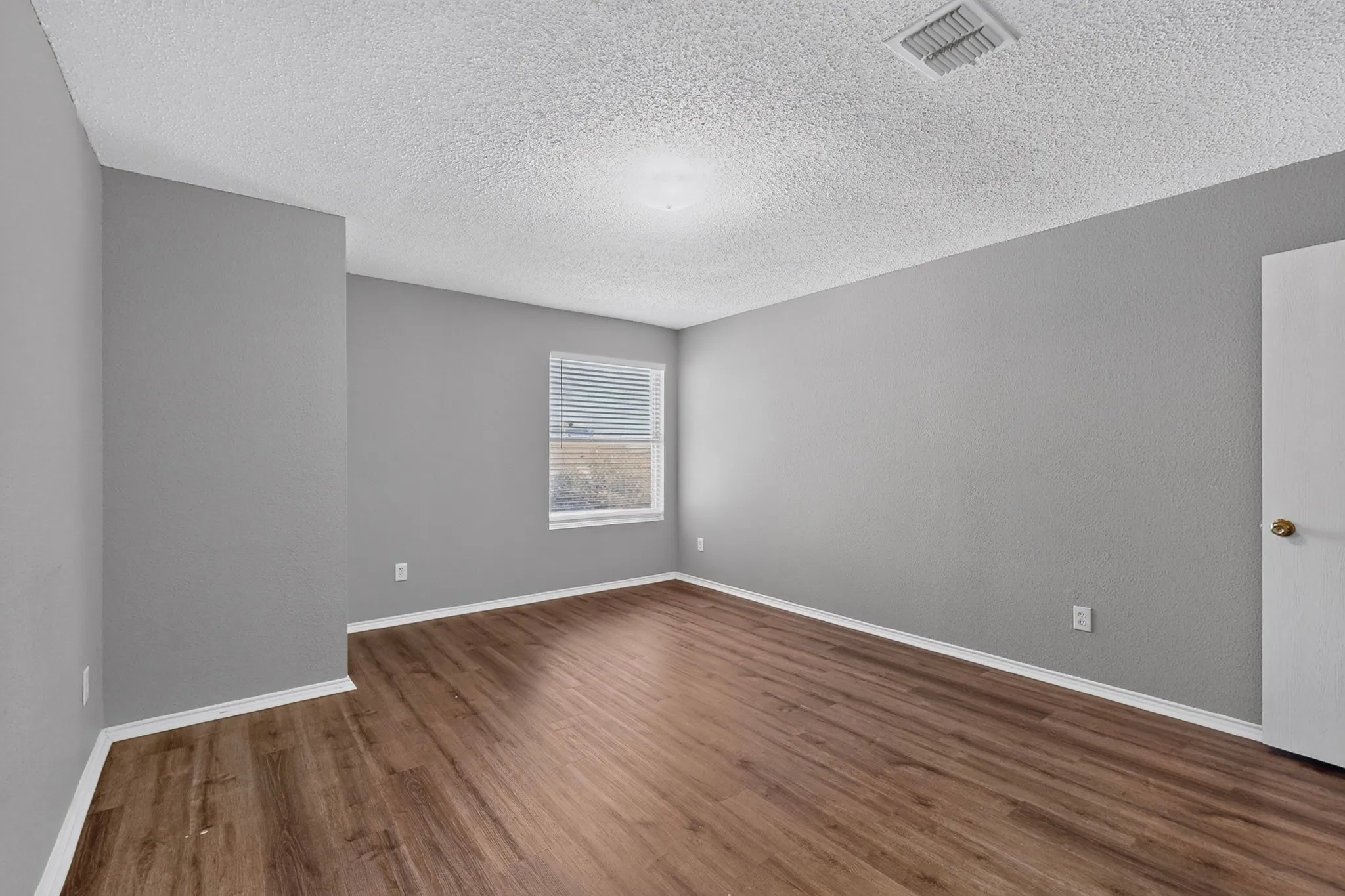 Wood-finish flooring, neutral gray wall tones, ceiling-mounted lighting, and a window with blinds