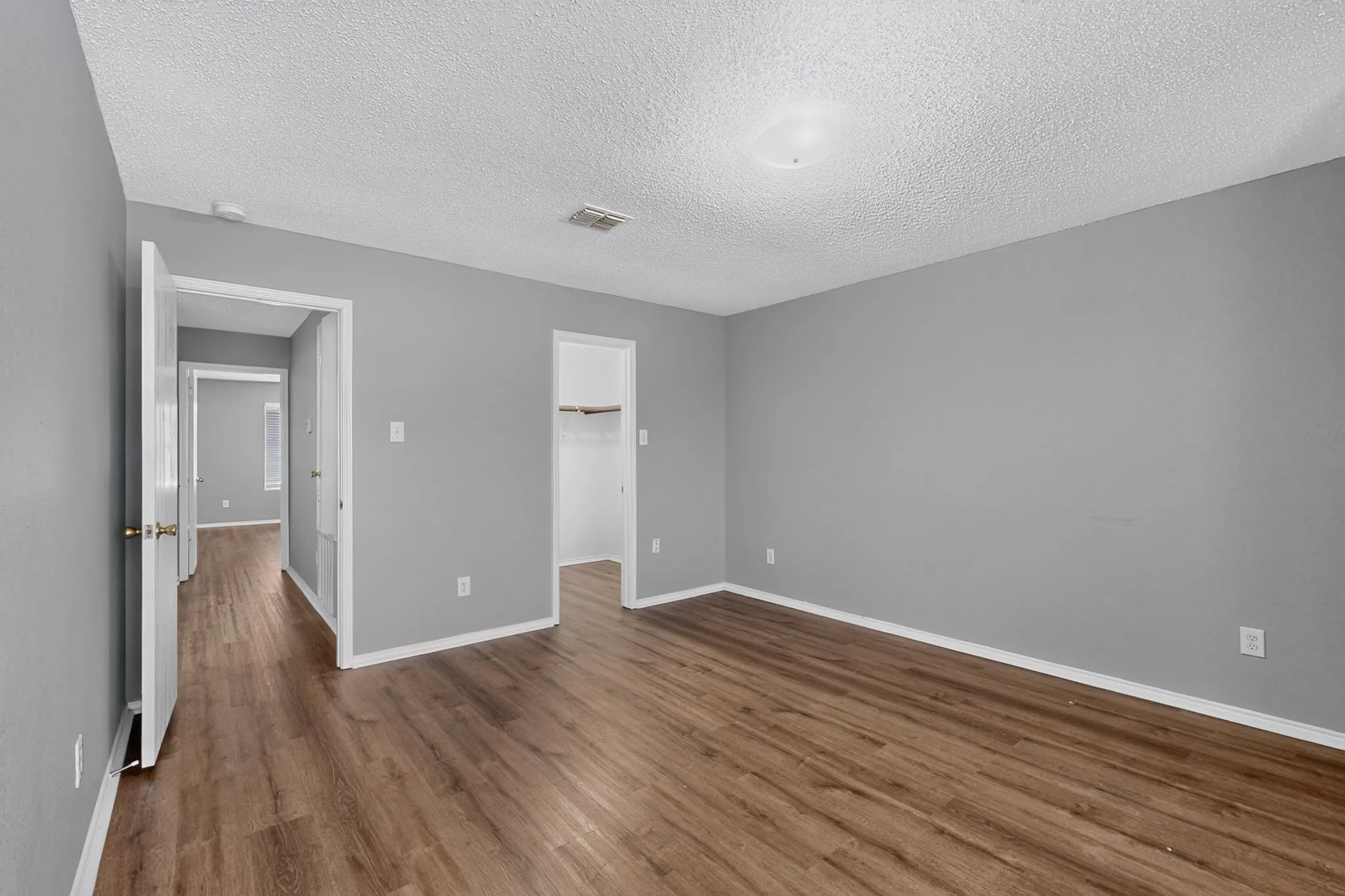 Spacious room featuring wood-finish flooring, light grey walls, and a built-in closet with shelving