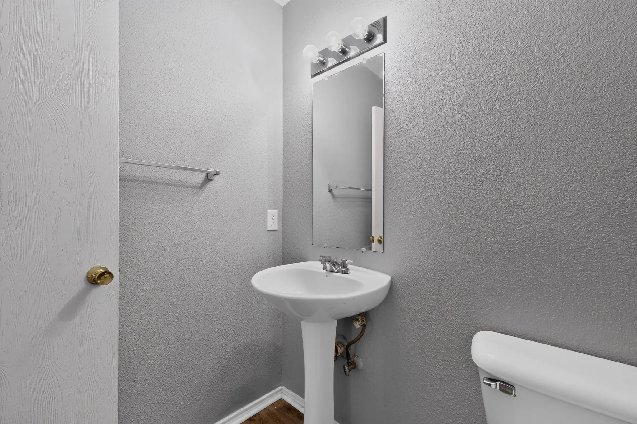 Pedestal sink with chrome faucet, wall-mounted mirror, and overhead vanity lighting