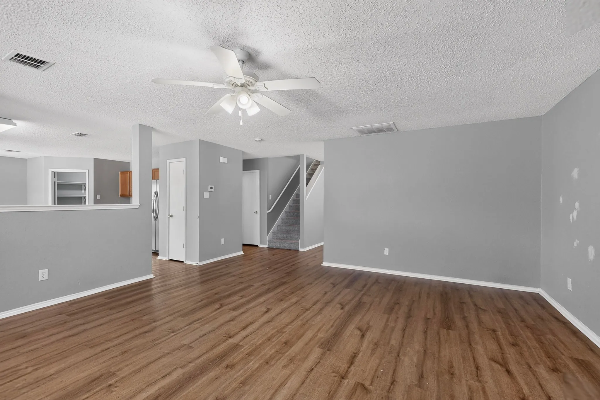 Wood-finish flooring throughout, ceiling fan with light fixture, gray painted walls, textured ceiling, and a staircase with carpeted treads
