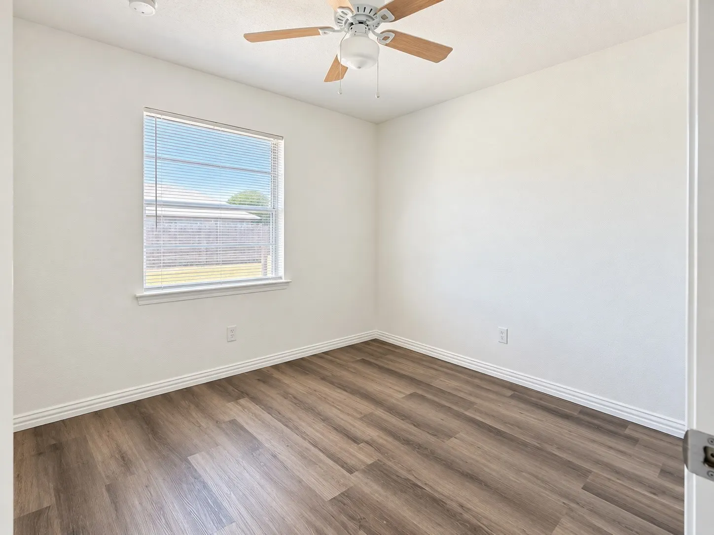 Wood-finish flooring, a window with horizontal blinds, a ceiling fan with light fixture, and white painted walls