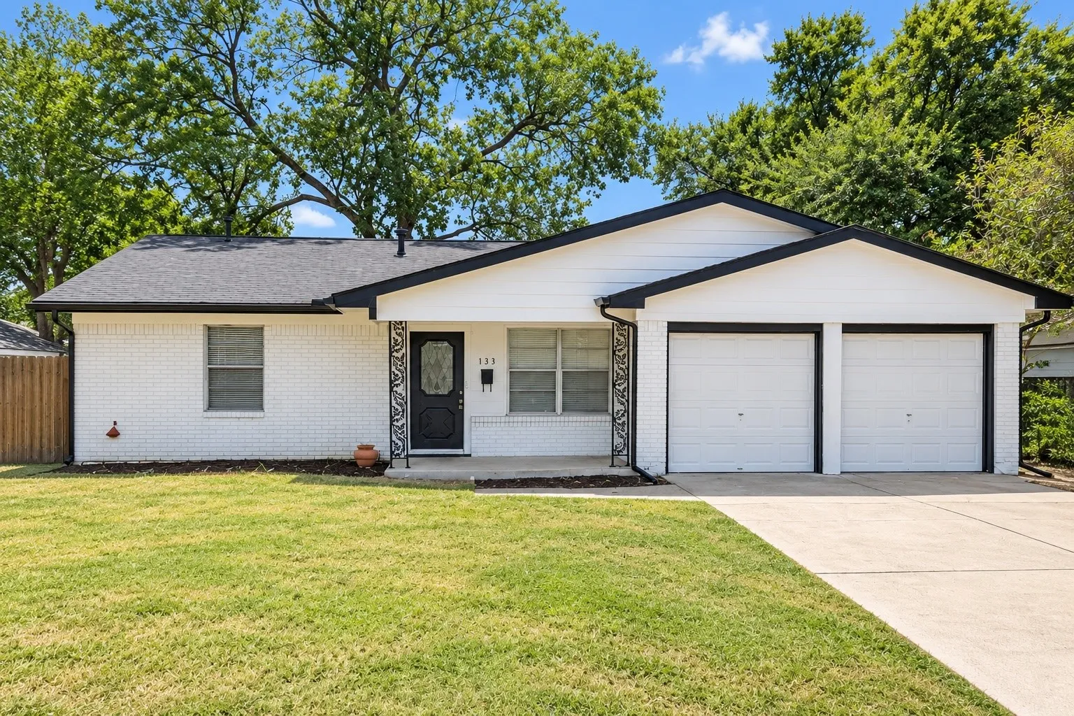 White brick exterior with black trim, a dark asphalt shingle roof, and a two-car garage