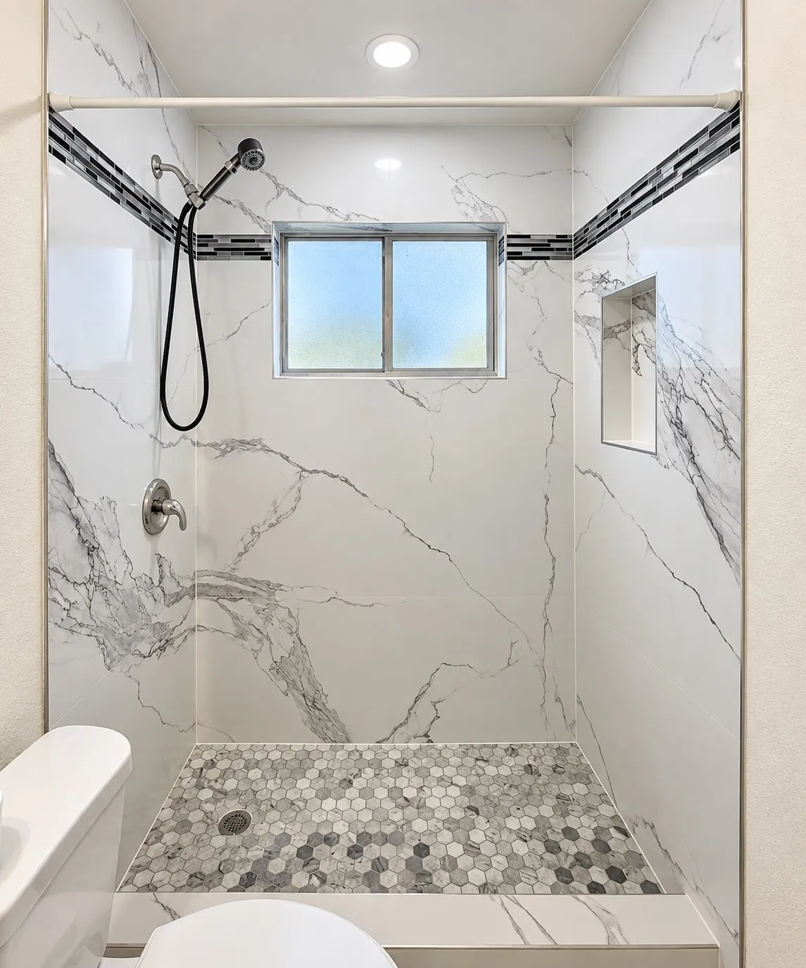 Shower with marble-look tile walls, mosaic hexagon floor, recessed lighting, and an integrated shower niche