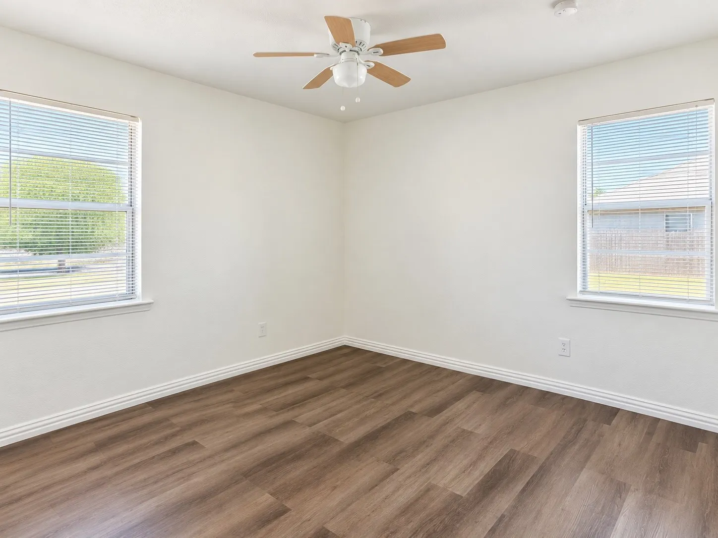 Light-filled room featuring two windows, wood-finish flooring, a ceiling fan, and white walls