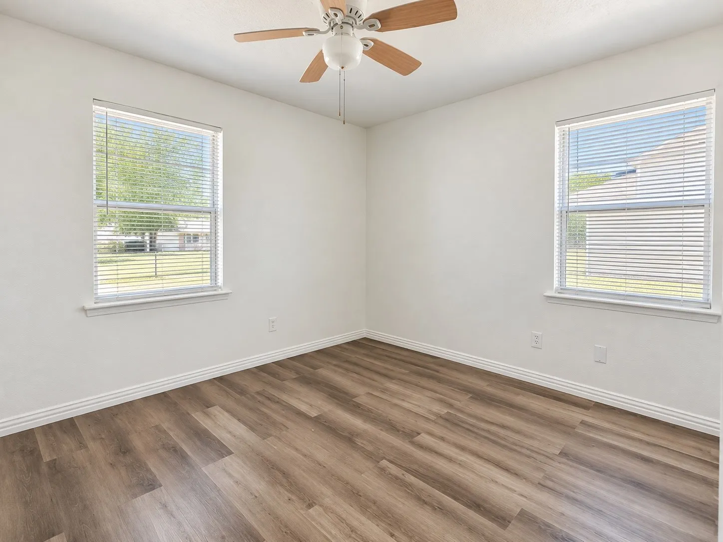 Wood-finish flooring, white walls, two windows with blinds, and a ceiling fan with integrated lighting