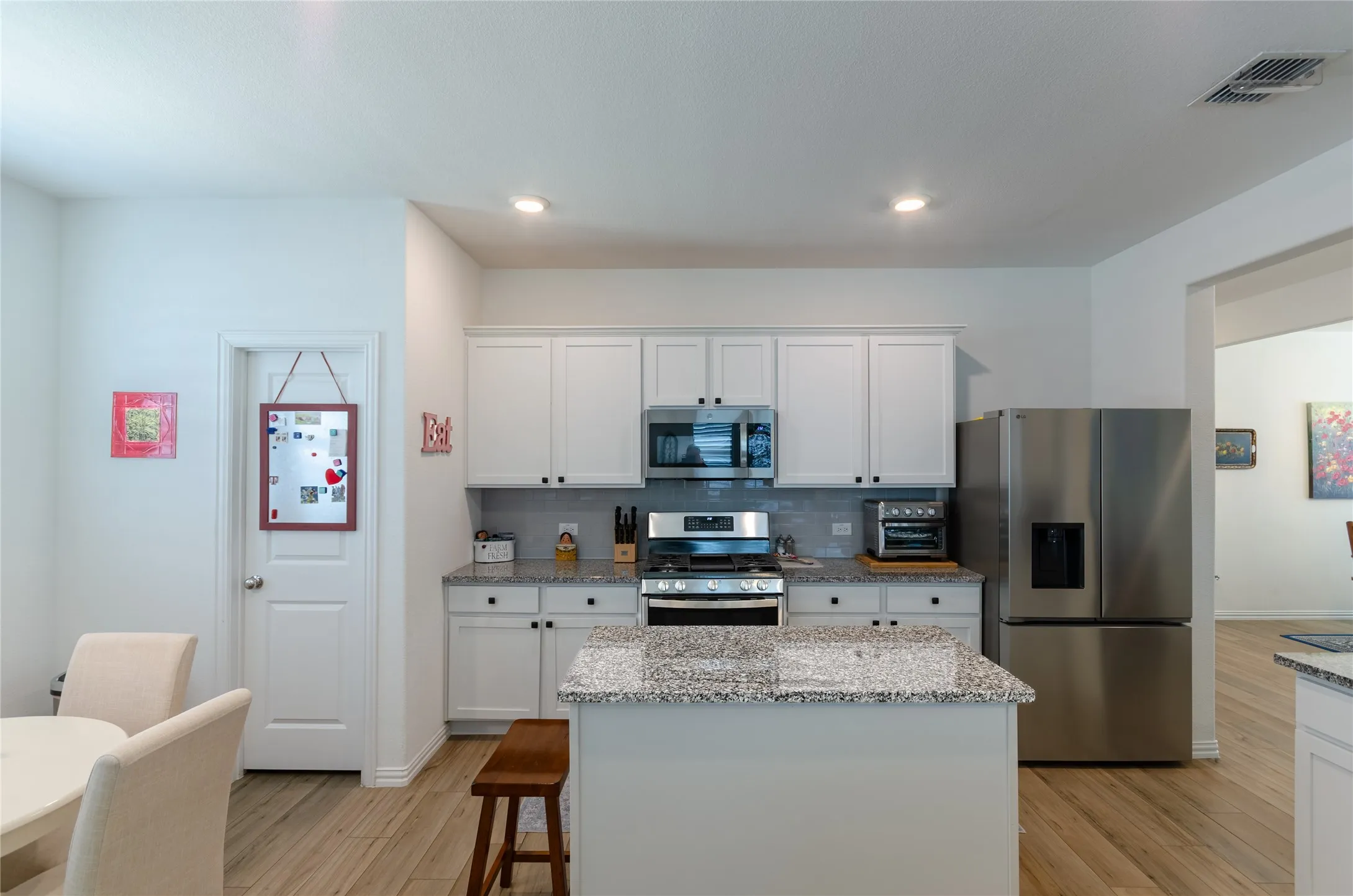 Kitchen featuring white cabinetry, stainless steel appliances, granite countertops, tile backsplash, and a central island