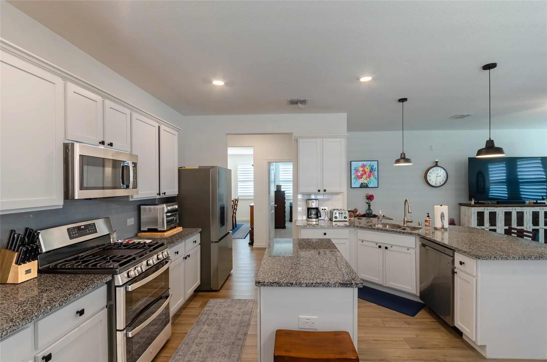Kitchen featuring white cabinetry, stainless steel appliances, granite countertops, a tile backsplash, and wood-finish flooring