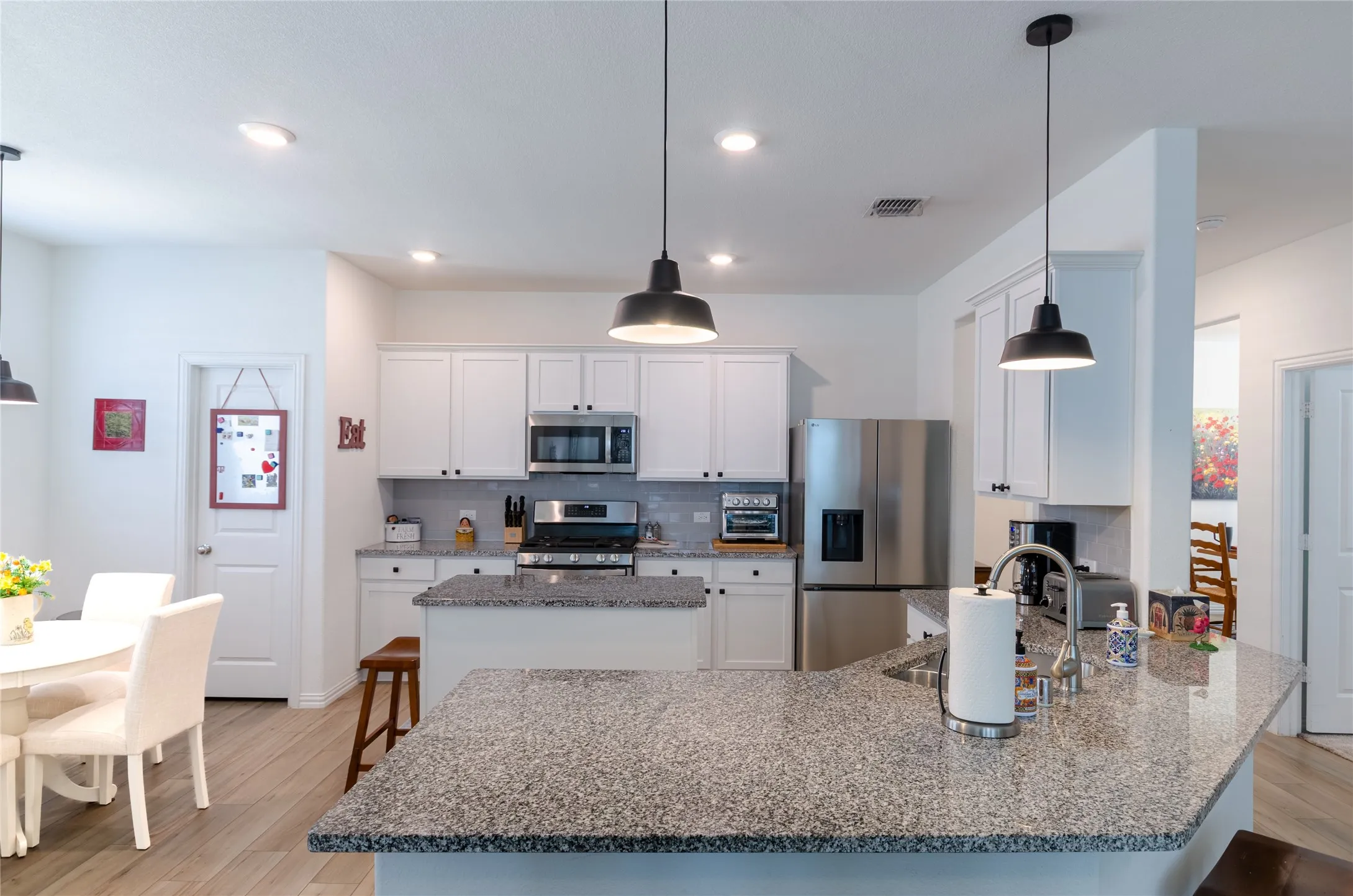 Modern kitchen featuring granite countertops, white cabinetry, stainless steel appliances, pendant lighting, and wood-finish flooring