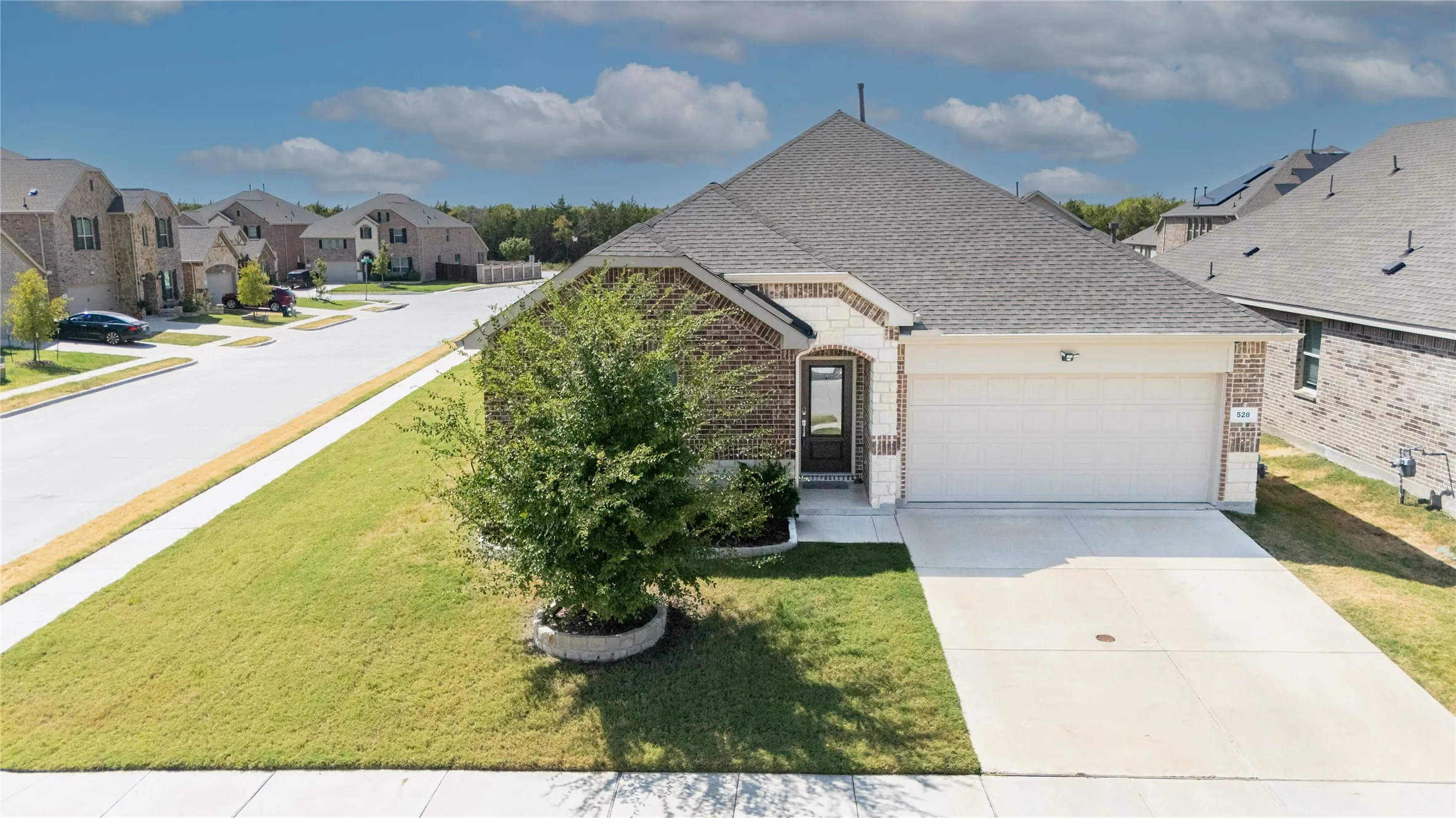 Brick and stone facade, attached two-car garage, concrete driveway, and a well-maintained front lawn