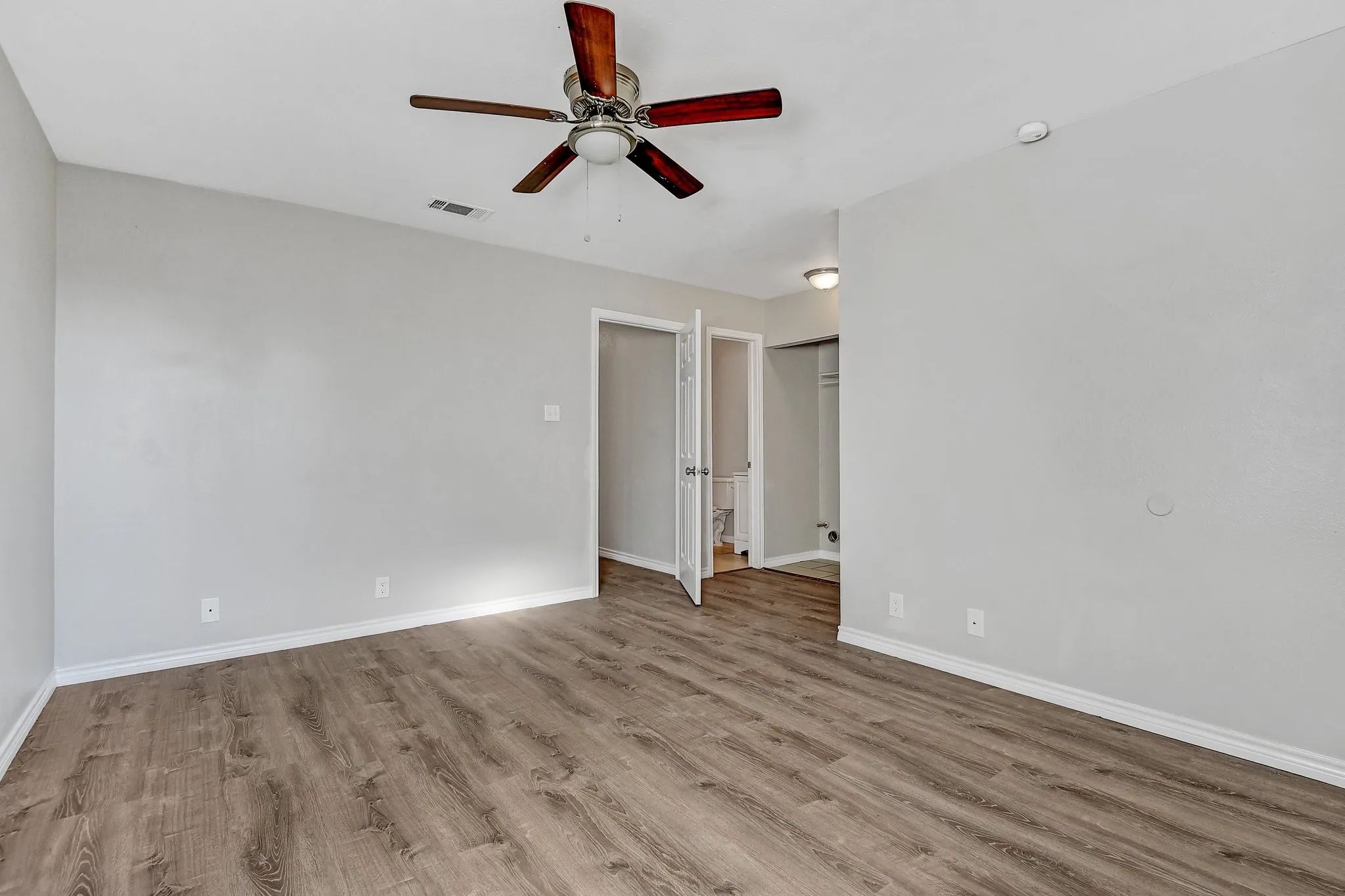 Unfurnished room with a ceiling fan, baseboards, visible vents, and wood finished floors