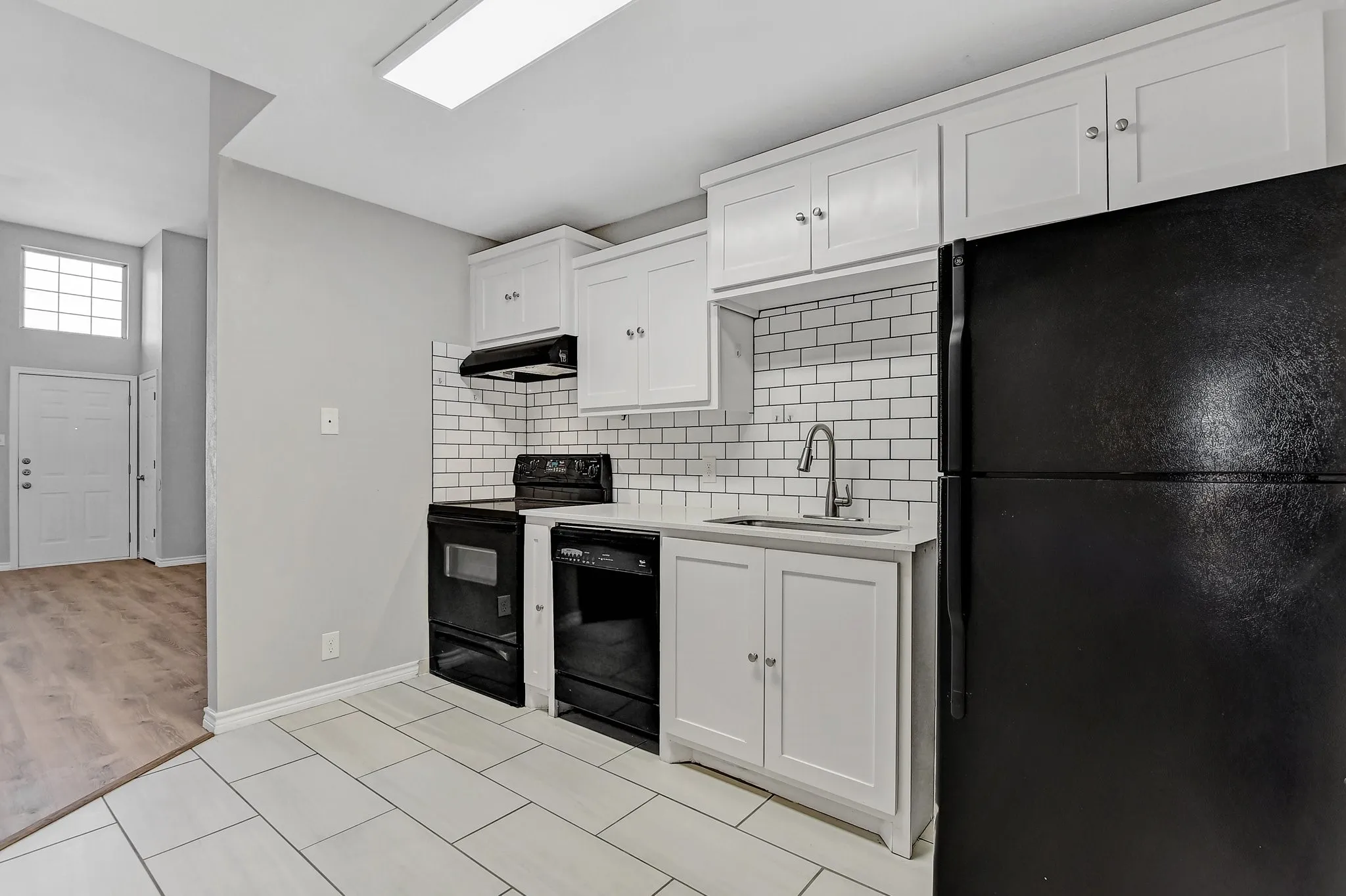 Kitchen with backsplash, a sink, light countertops, black appliances, and under cabinet range hood