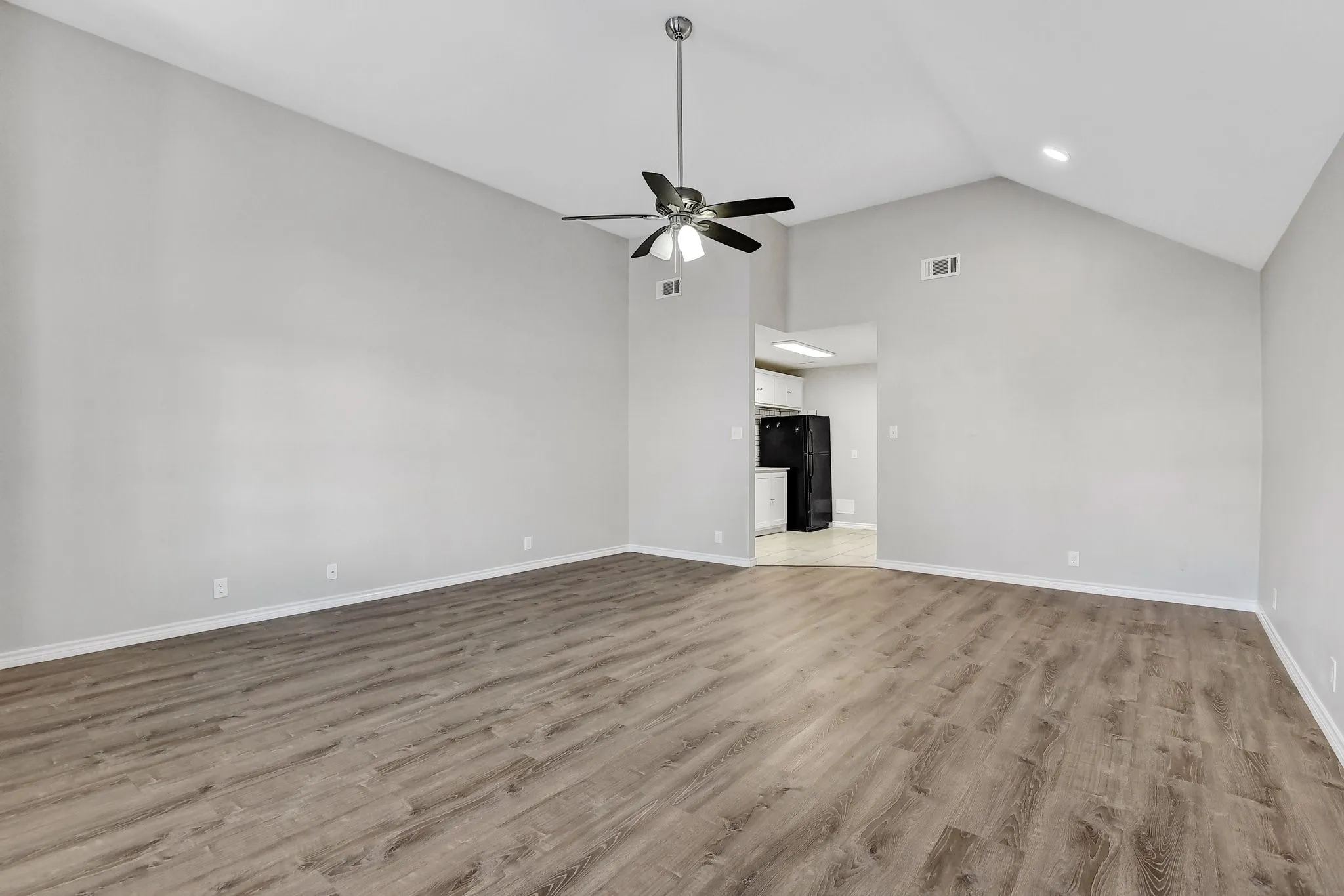 Unfurnished living room featuring high vaulted ceiling, a ceiling fan, light wood finished floors, and visible vents