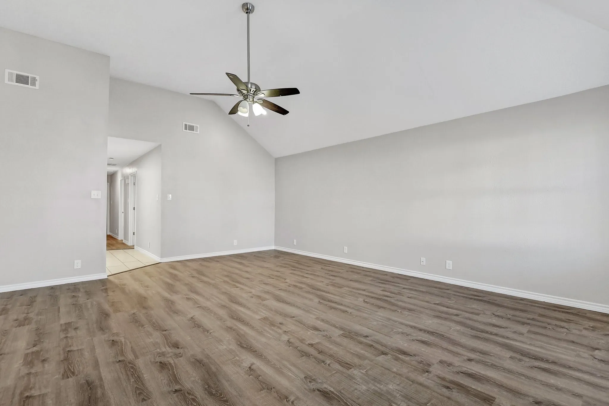 Unfurnished living room featuring visible vents, wood finished floors, baseboards, a ceiling fan, and vaulted ceiling