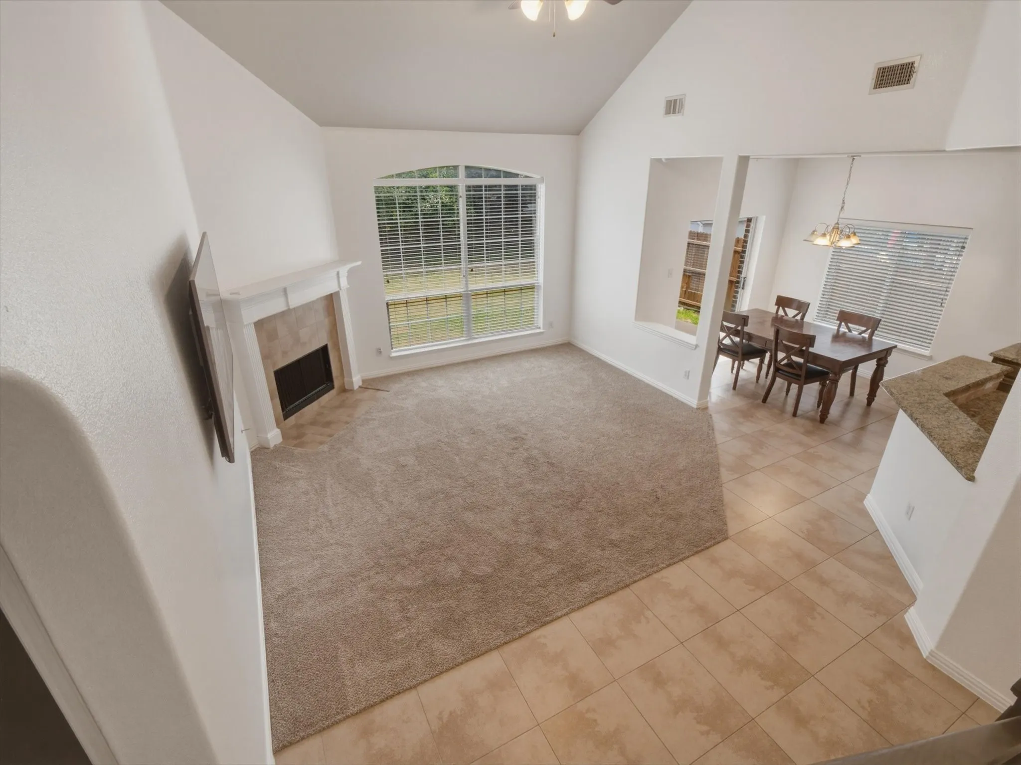 Vaulted ceiling living area with carpet flooring, arched window, and a fireplace with a mantel