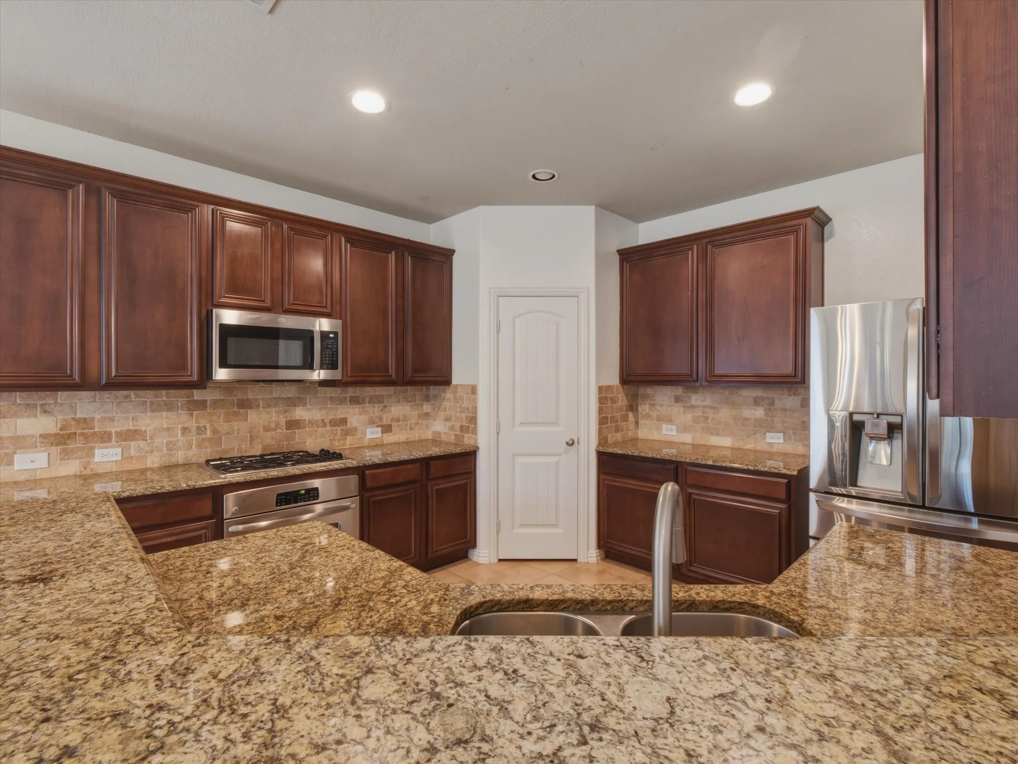 Kitchen featuring granite countertops, wood cabinetry, stainless steel appliances, a tile backsplash, and recessed lighting