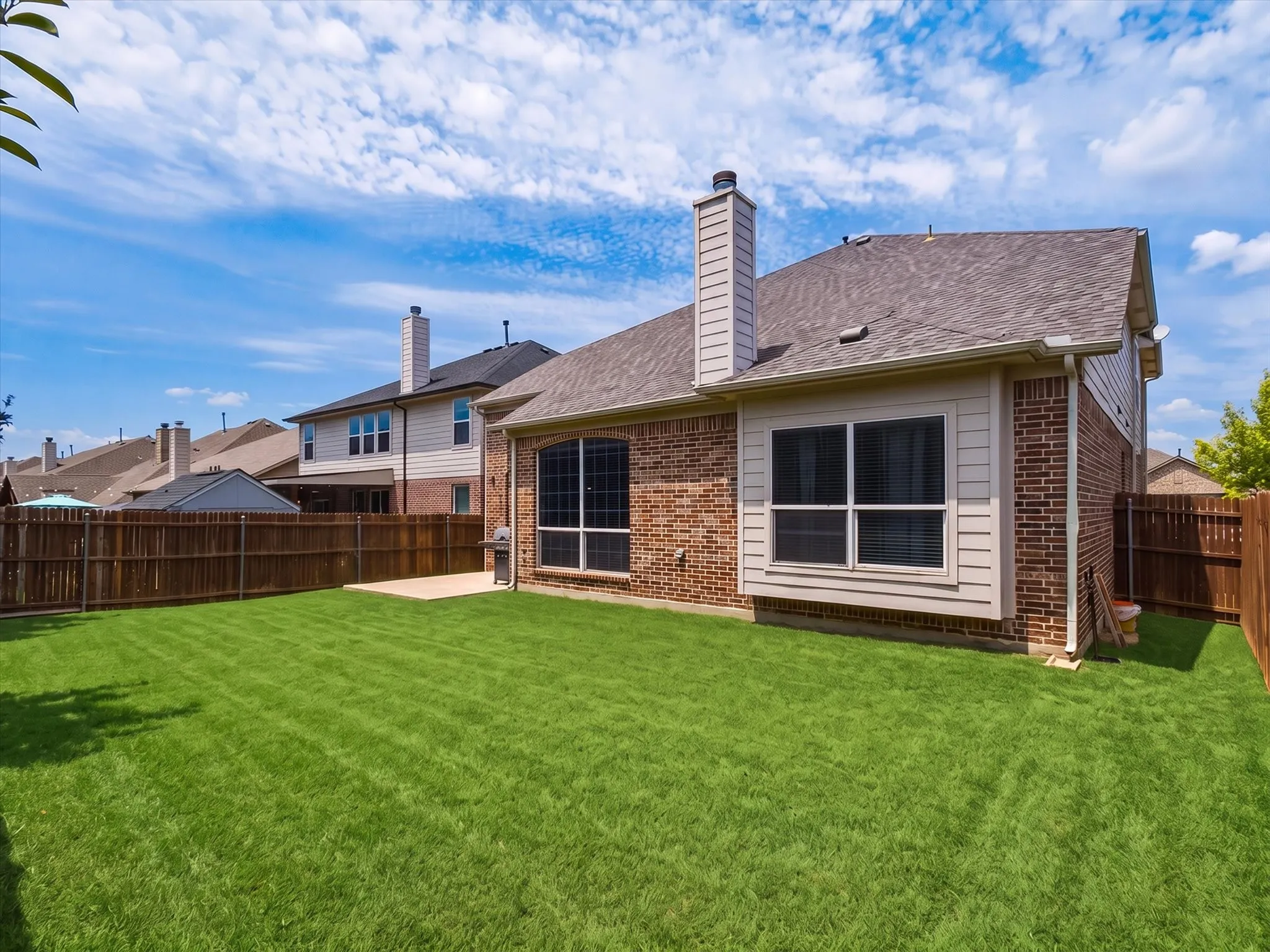 Expansive green lawn, wood fence perimeter, brick exterior, bay window, and a patio area