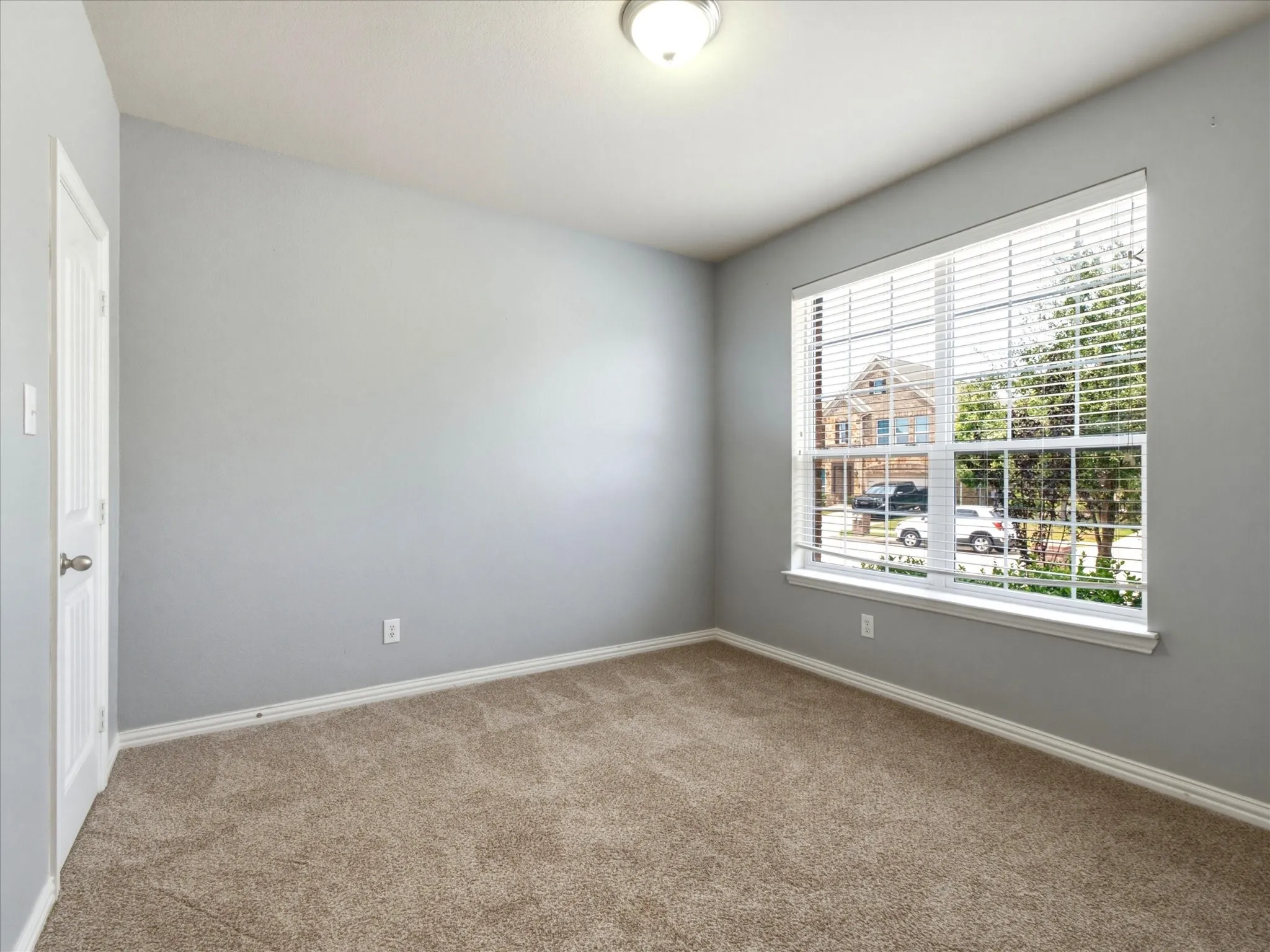 Neutral-toned wall paint, carpet flooring, a single window with blinds, and a flush mount light fixture