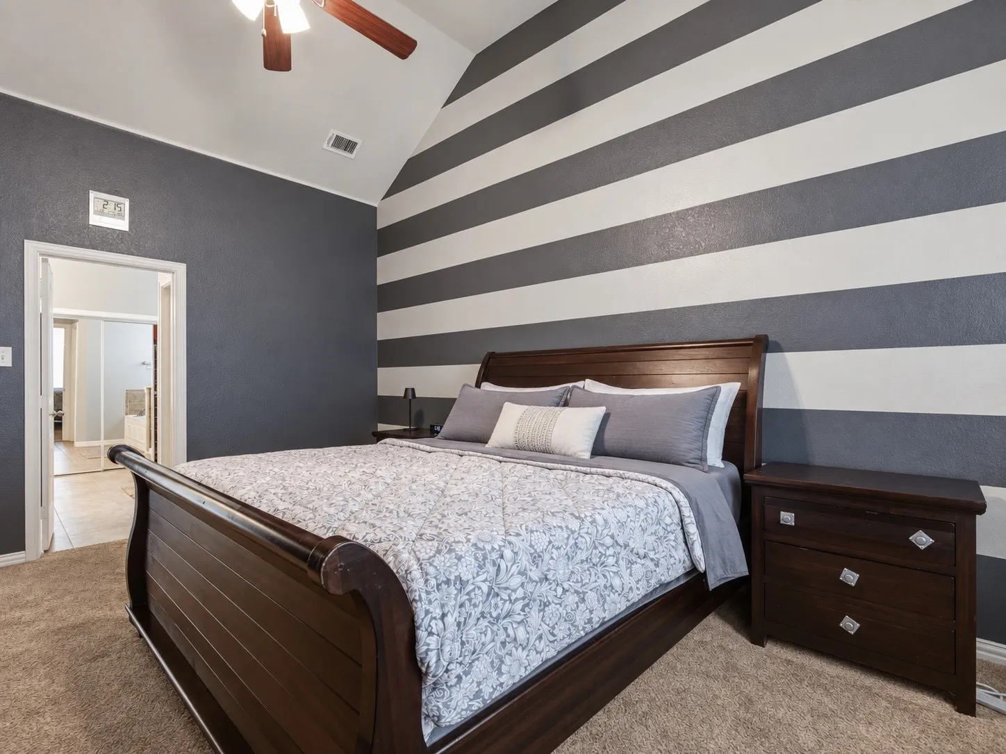 Vaulted ceiling with a ceiling fan, accent wall with horizontal stripes, and carpeted flooring