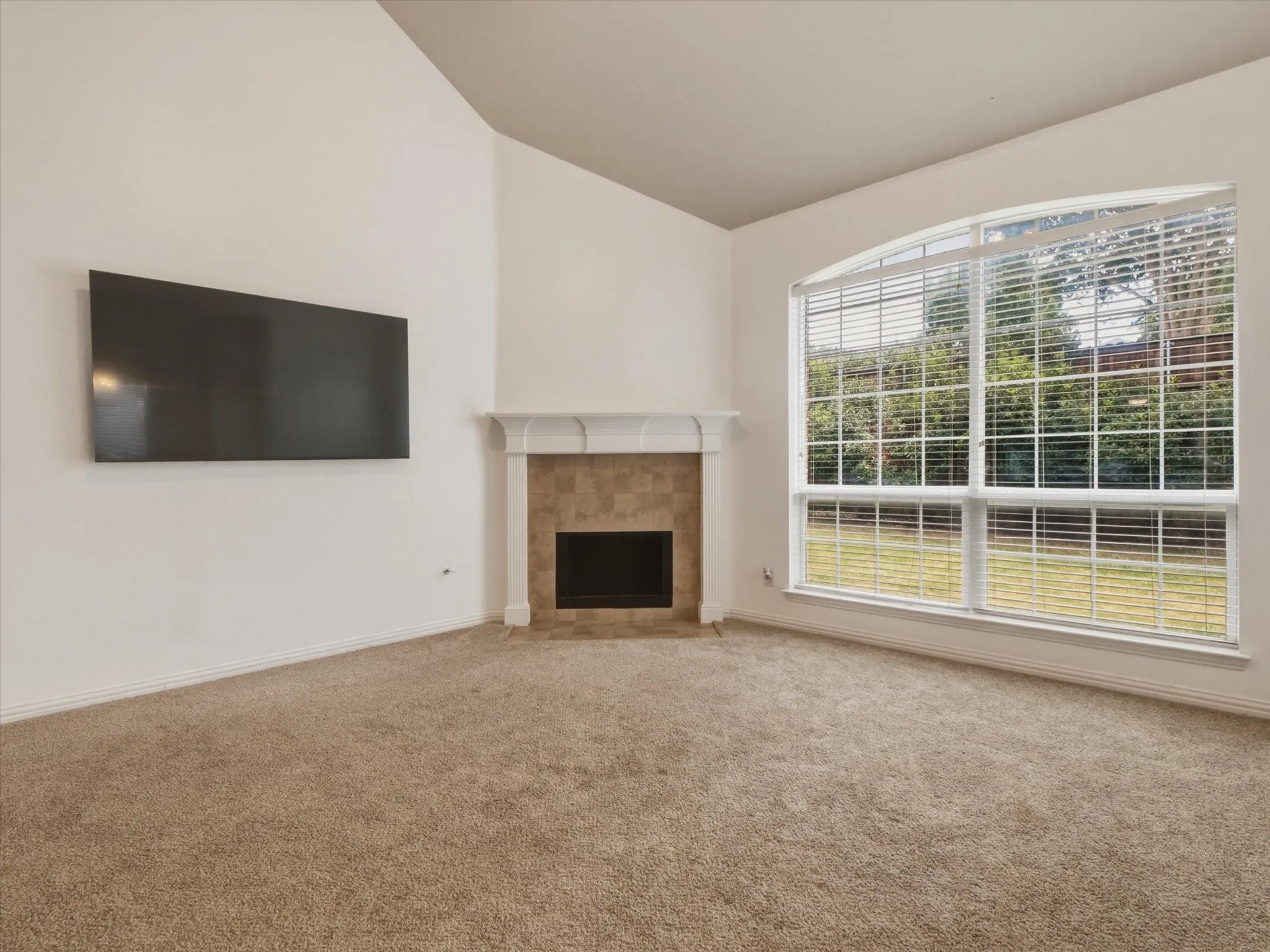 Vaulted ceiling room, built-in fireplace featuring stone tile, carpet flooring