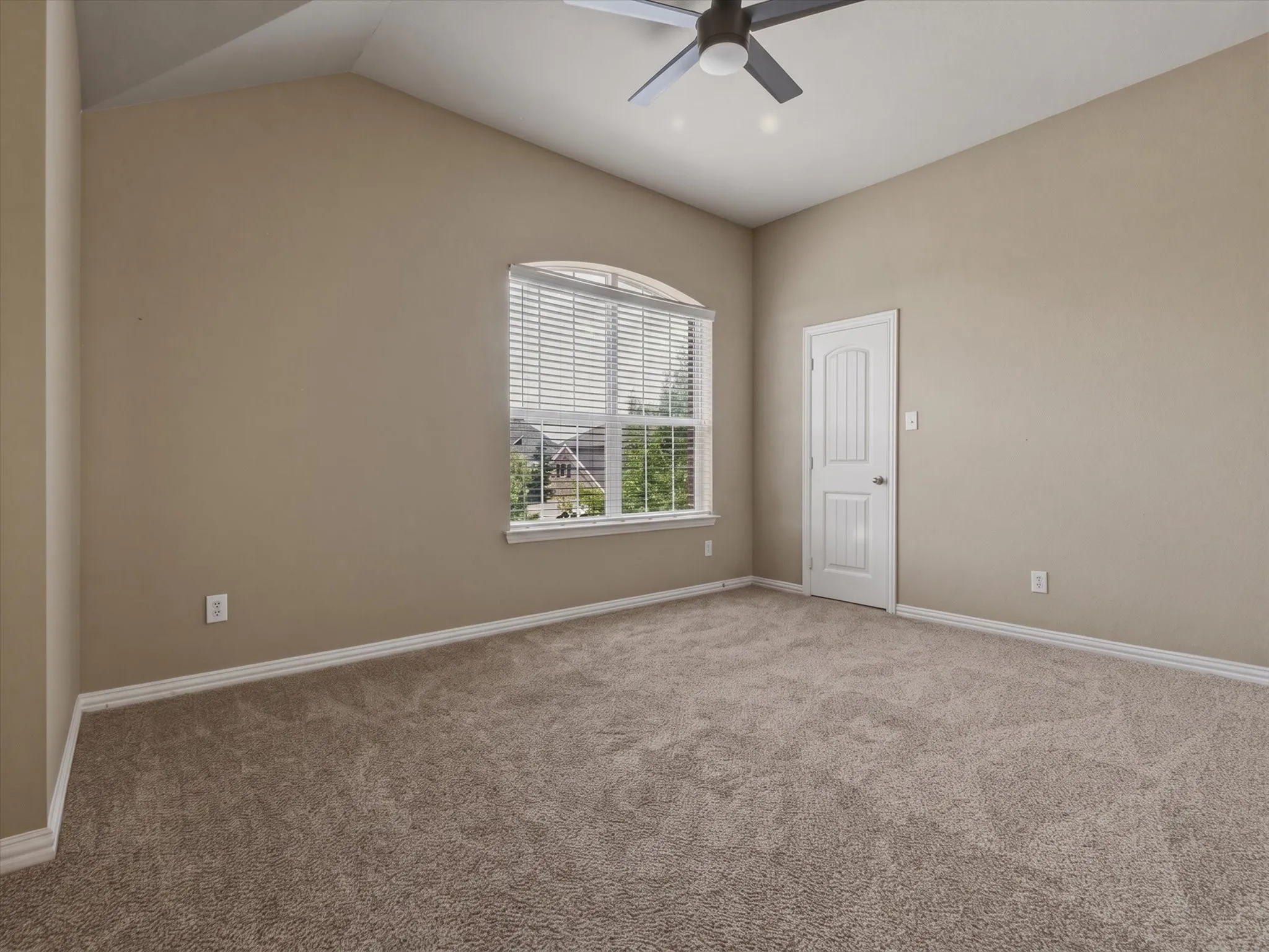 Vaulted ceiling with a ceiling fan, arched window with horizontal blinds, neutral-toned carpet, and a paneled interior door
