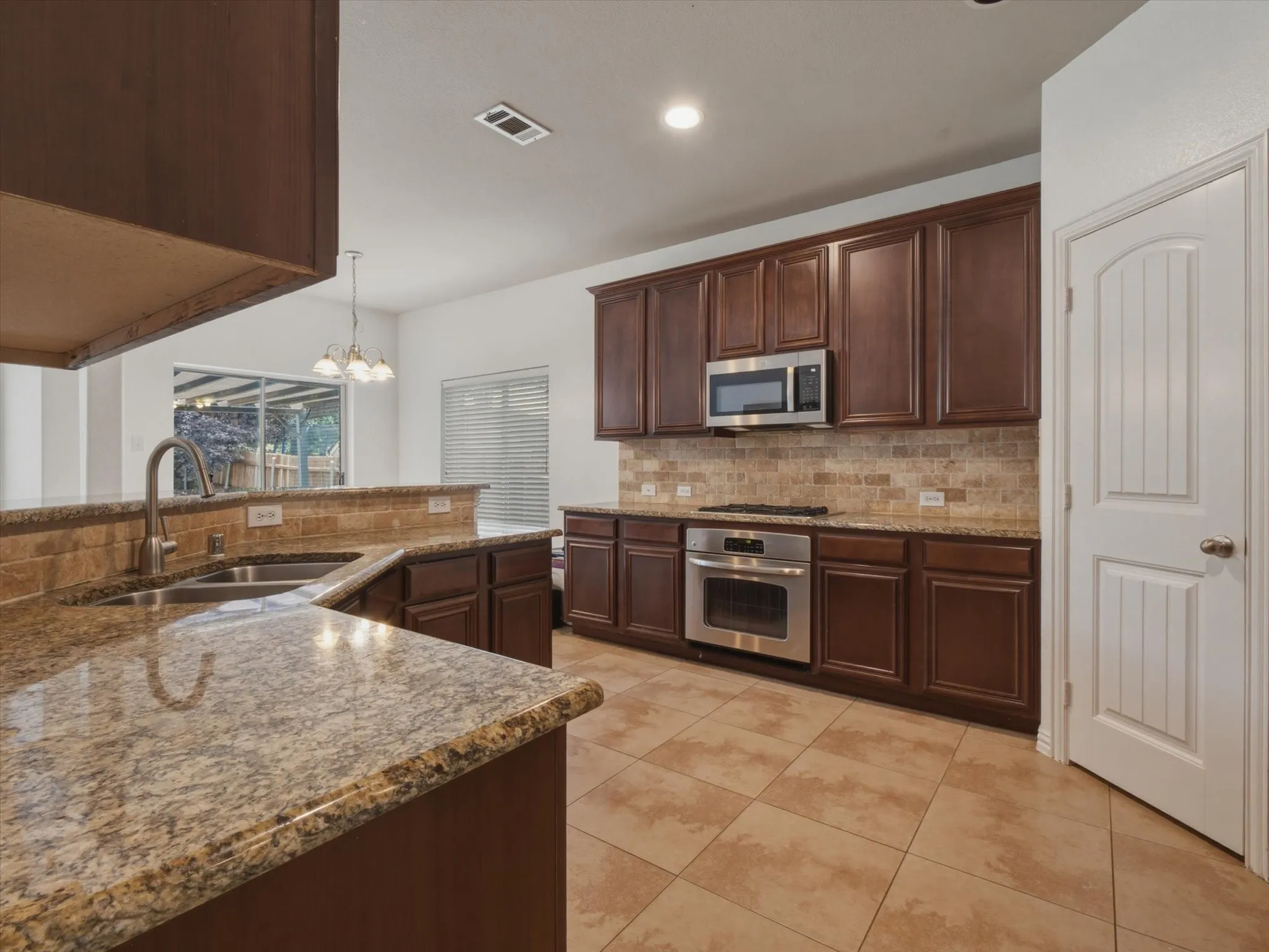 Kitchen featuring dark wood cabinetry, light granite countertops, stainless steel appliances, and a tiled backsplash