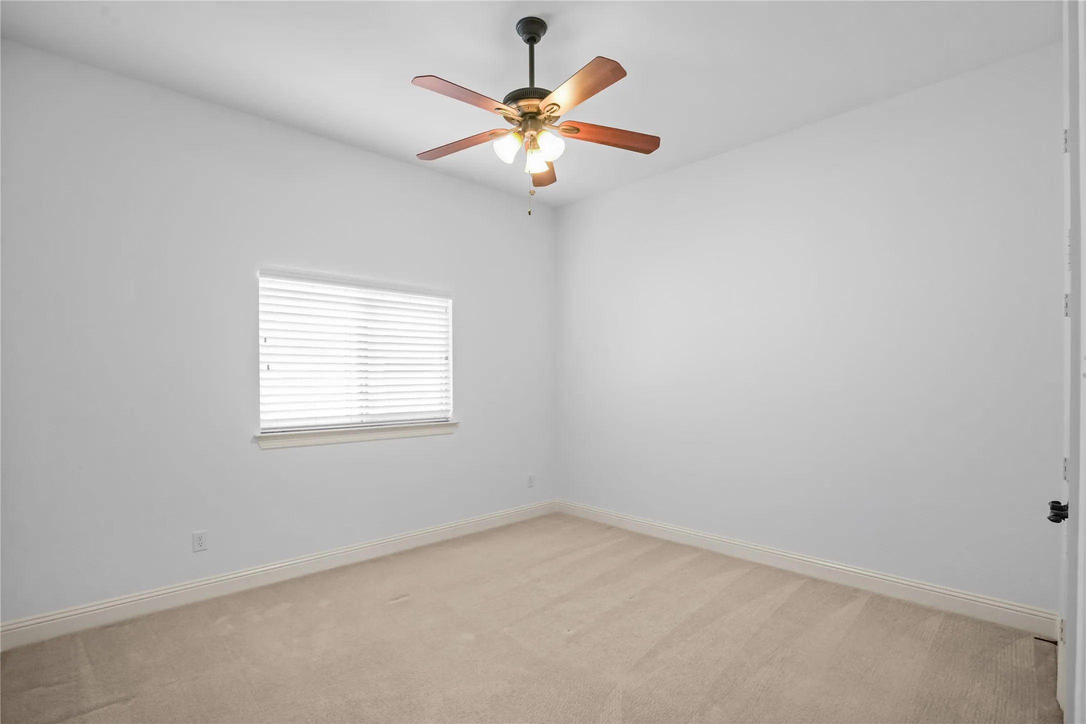 Light-filled interior featuring neutral wall tones, carpet flooring, a ceiling fan with integrated lighting, and a window with horizontal blinds