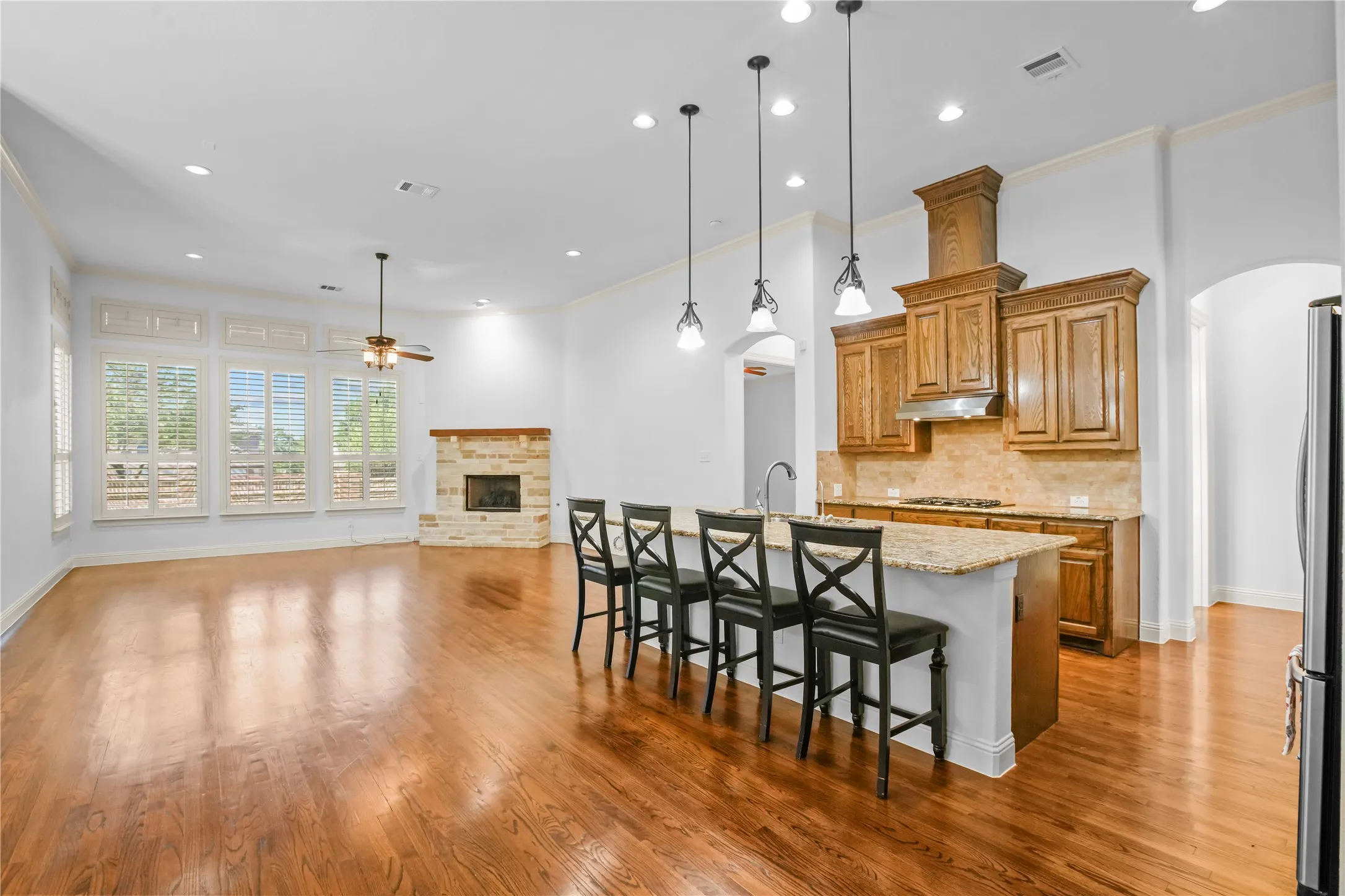 Hardwood flooring, stone fireplace, kitchen island with seating, pendant lighting, and custom cabinetry