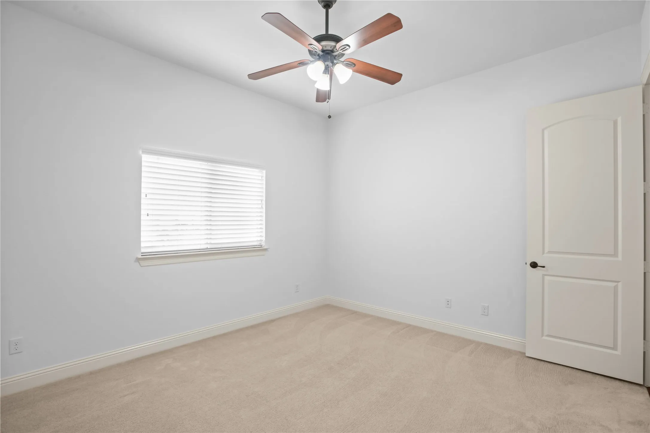Ceiling fan with light fixture, window with blinds, light-toned carpet flooring, white walls, and a white arched panel door with dark hardware