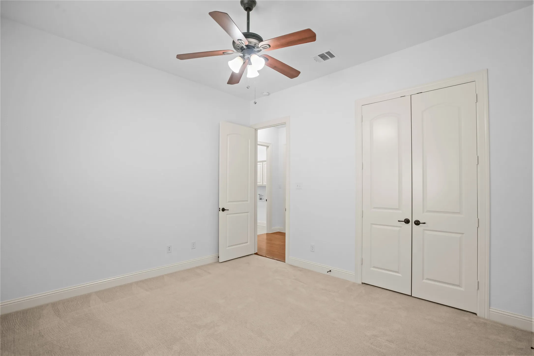 Plush carpeted flooring, a ceiling fan with integrated lighting, and white walls
