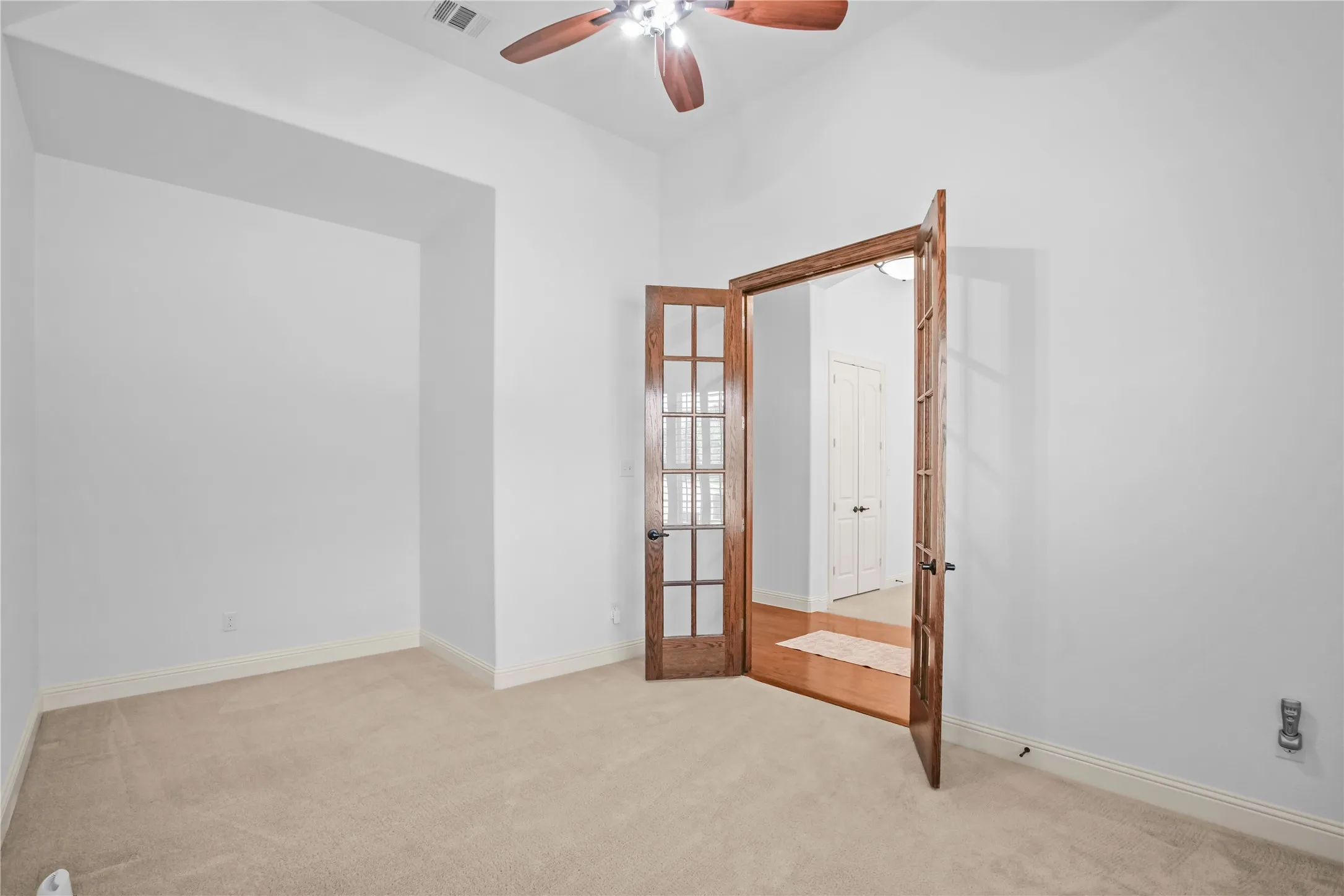 Carpeted study with high ceilings, recessed wall niche, and wood-finish French doors