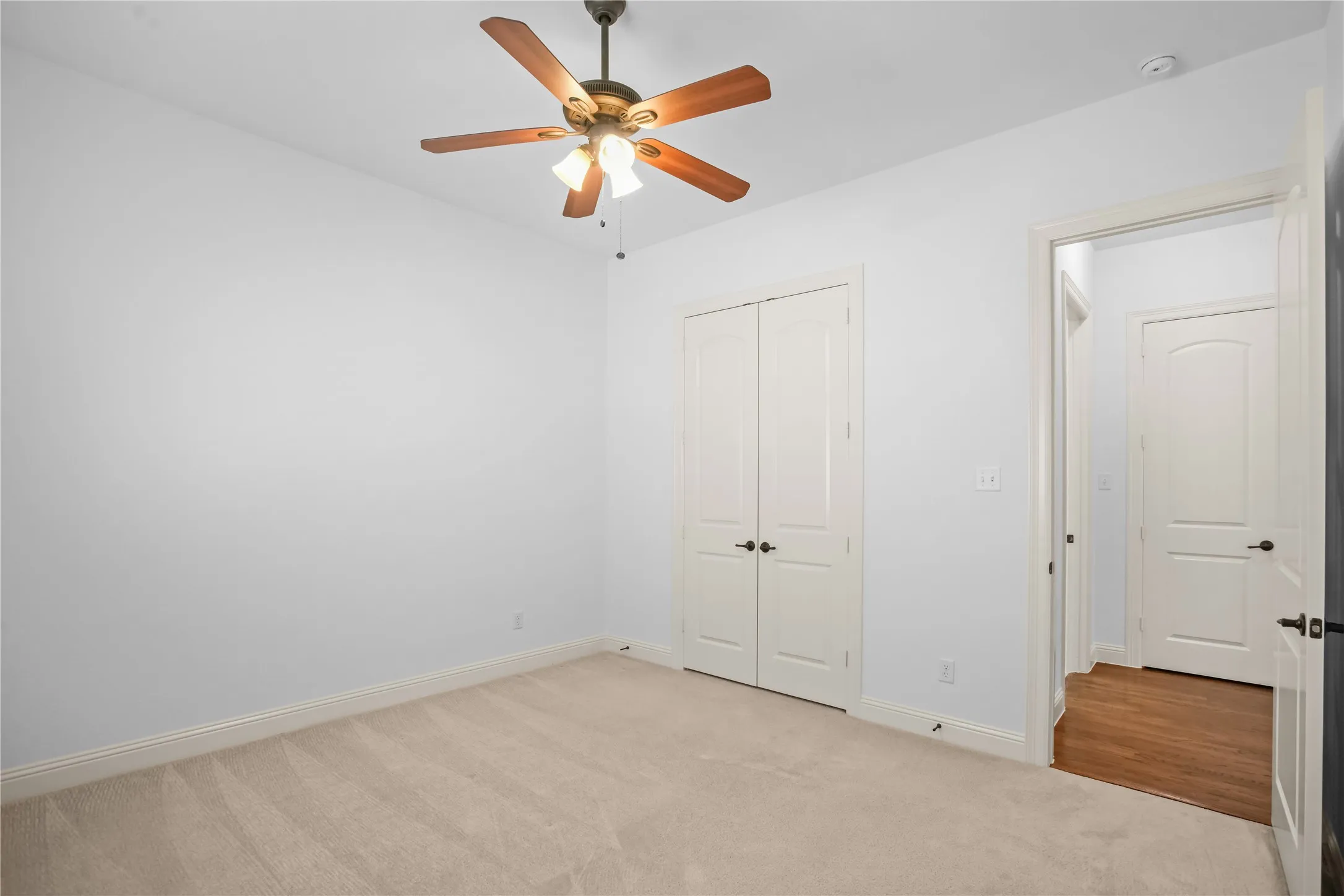 Neutral carpet flooring, bi-fold closet doors, ceiling fan with integrated lighting, wood-finish flooring visible through doorway
