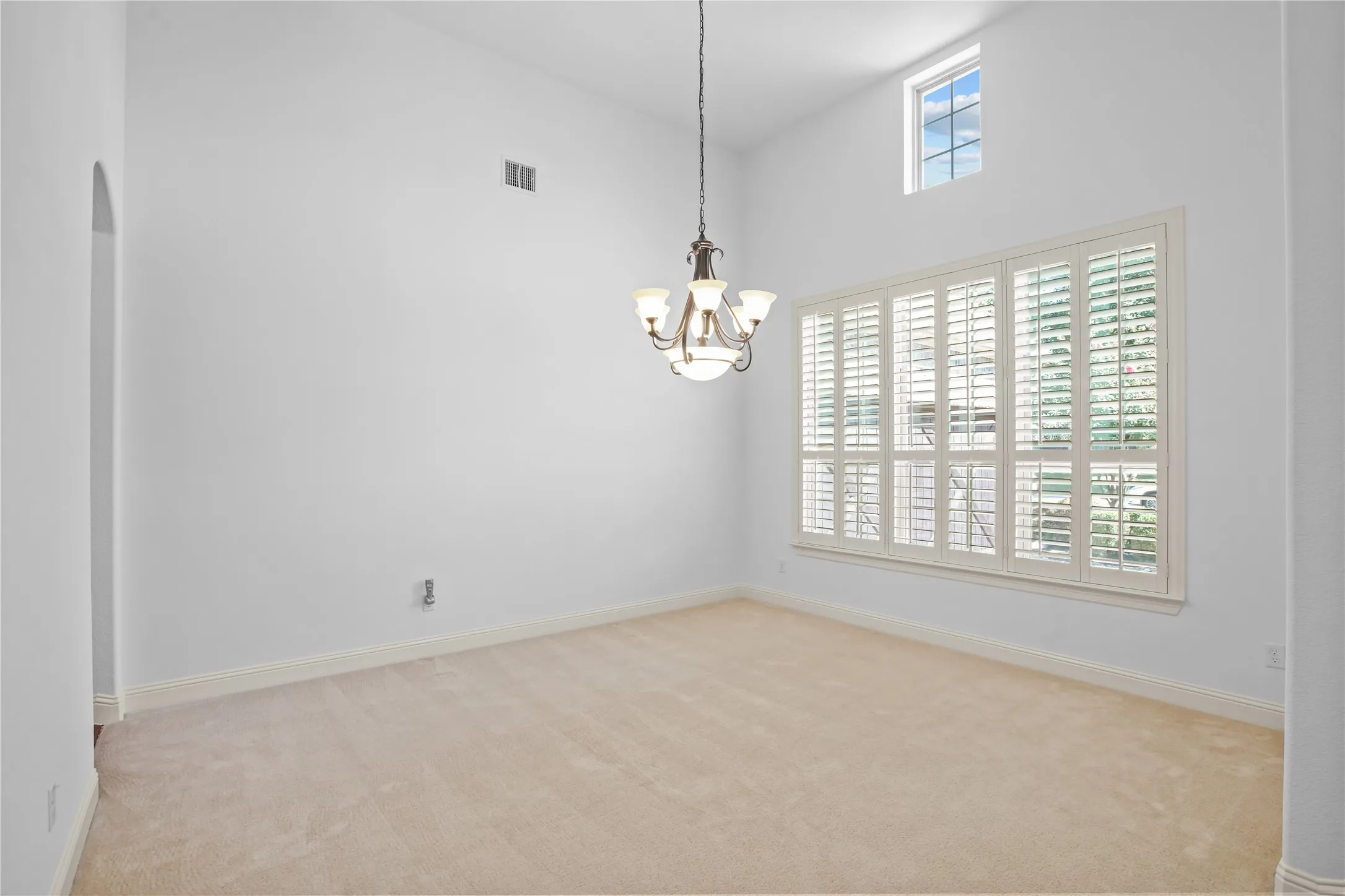 Vaulted ceiling with an arched entry, chandelier, and a large window featuring plantation shutters