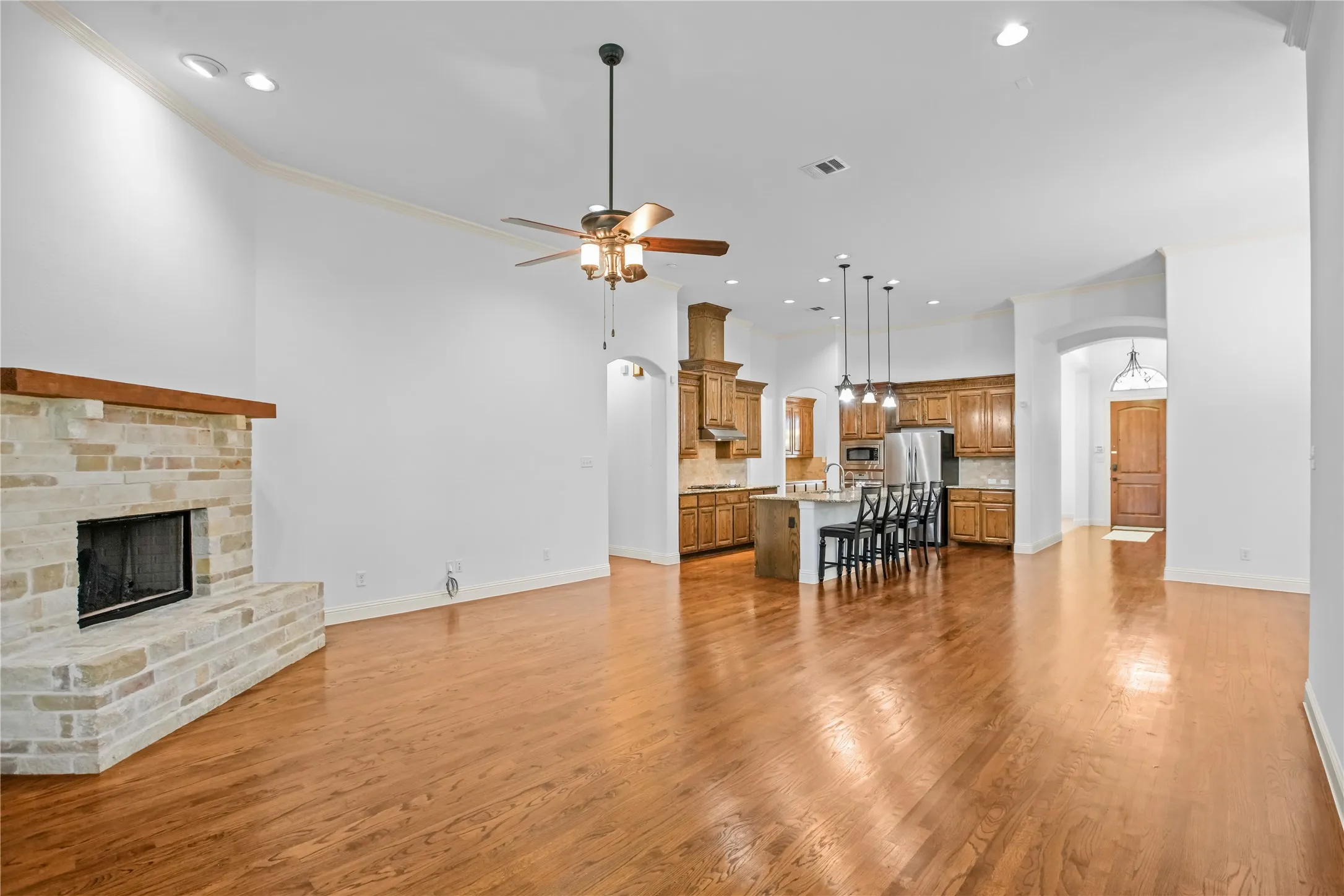 Stone-clad fireplace with wood mantle, vaulted ceiling with recessed lighting, wood-finish flooring, kitchen with built-in cabinetry, and kitchen island with pendant lighting