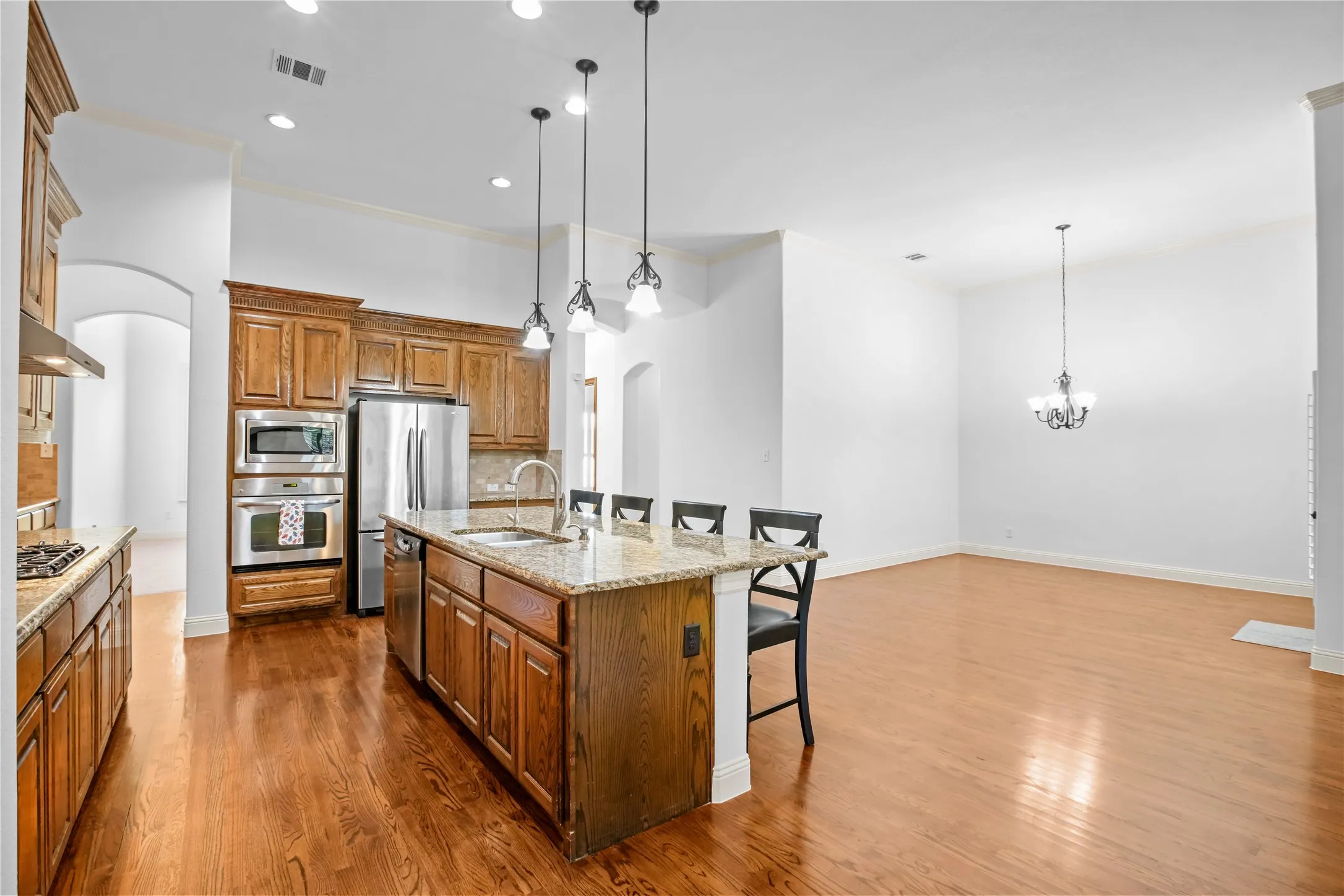 Wood-finish flooring throughout, kitchen island with granite countertop, stainless steel appliances, pendant lighting, and recessed ceiling lights