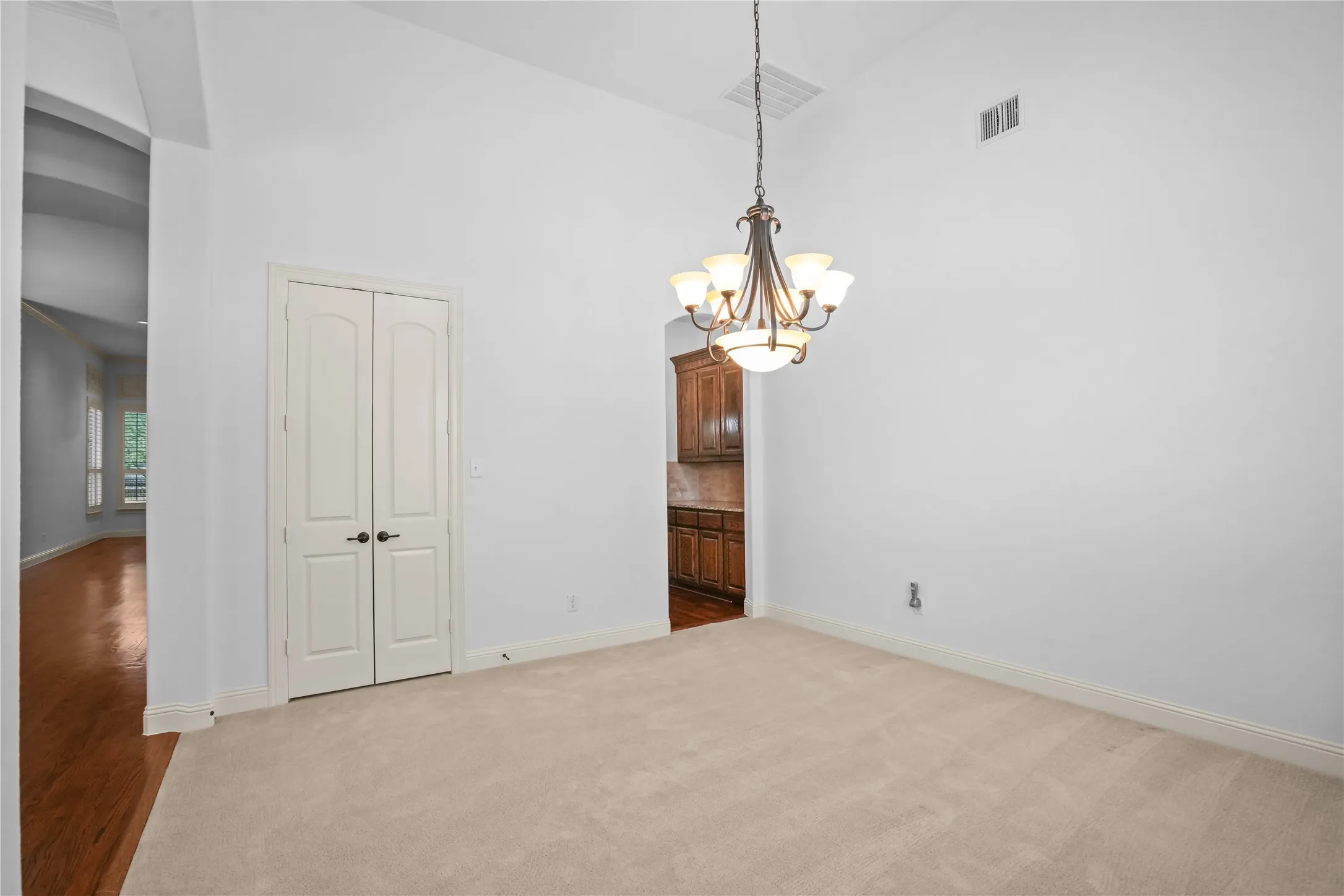 Vaulted ceiling, carpeted flooring, double panel doors, and a chandelier lighting fixture