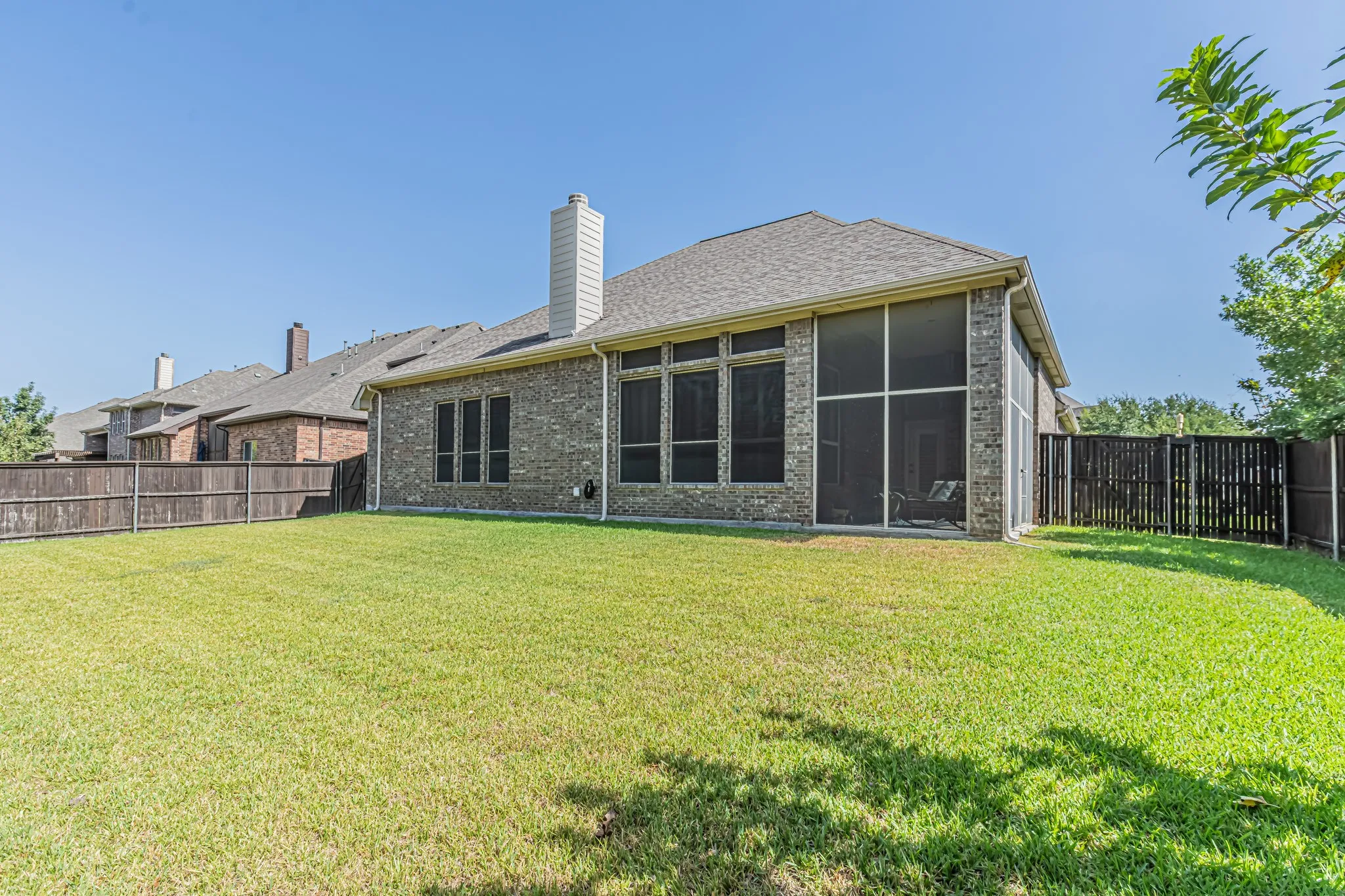 Brick exterior with a screened-in patio, multiple window openings, and a fenced backyard