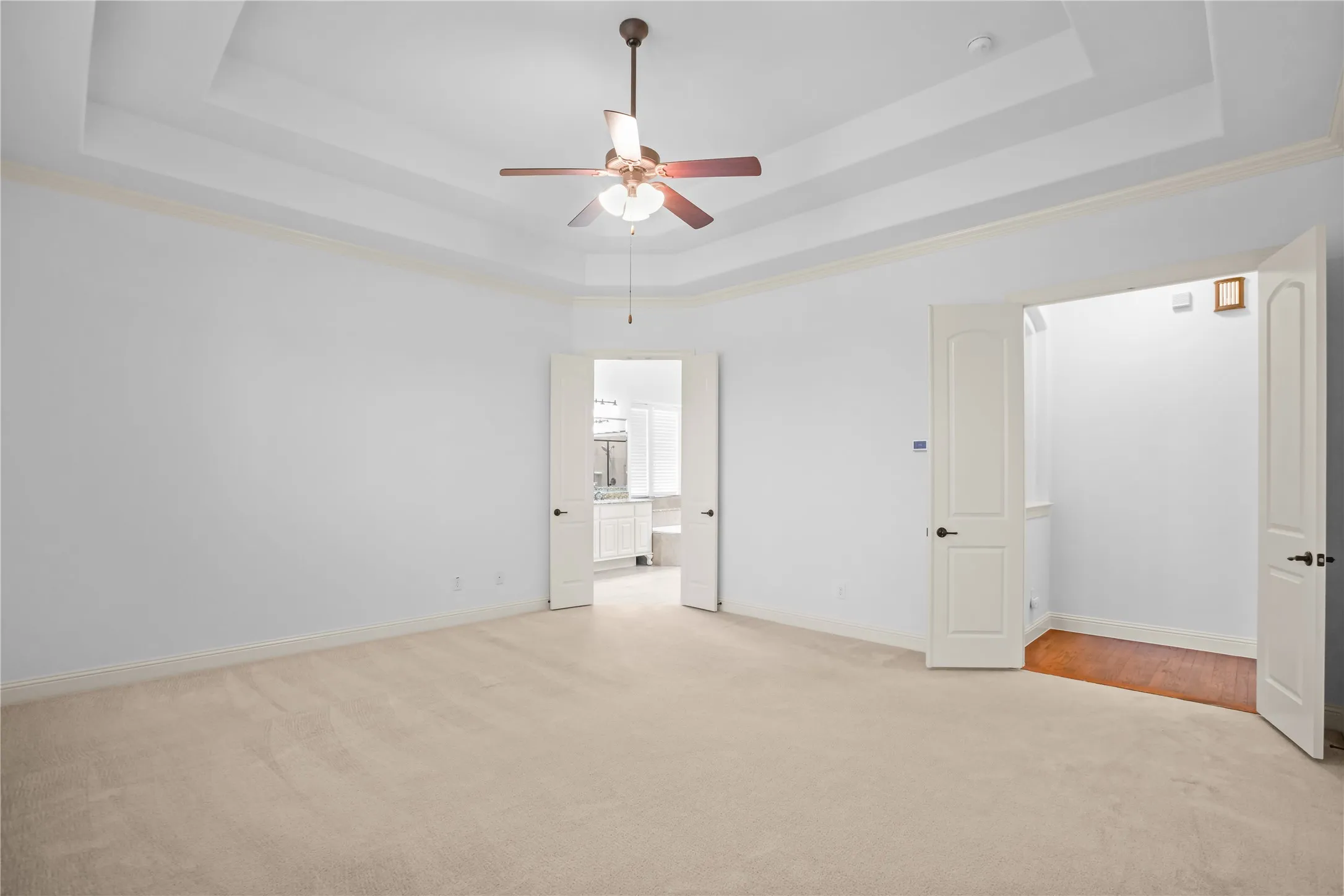 Tray ceiling with crown molding, ceiling fan, and carpeted flooring