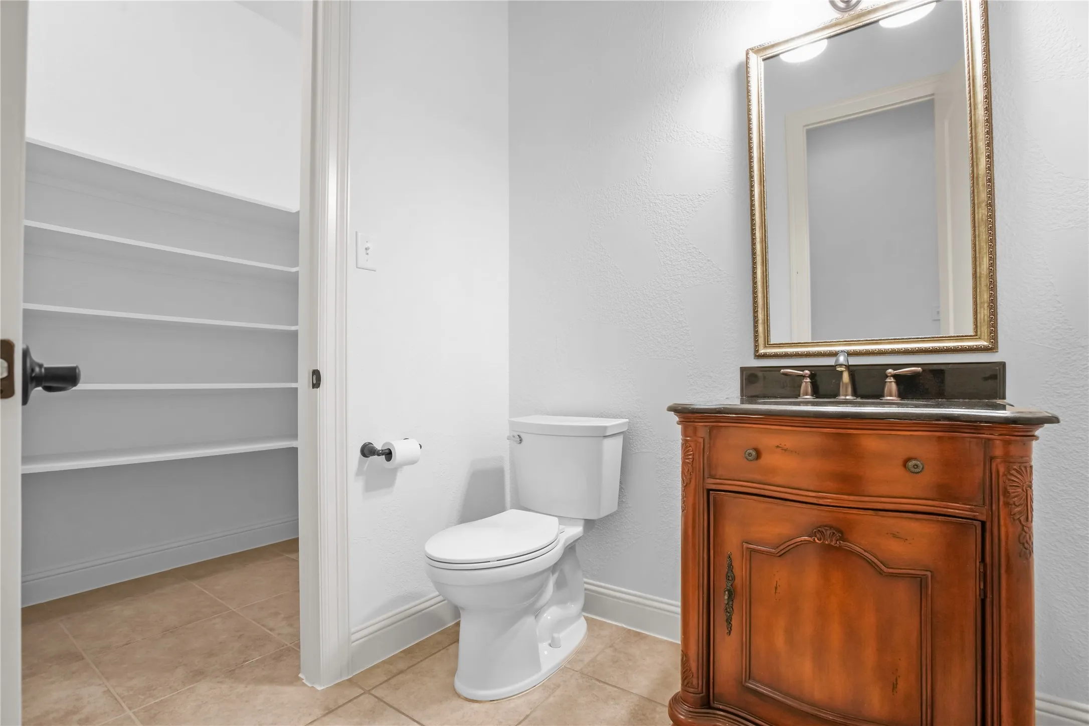 Tile flooring, built-in shelving, vanity with integrated sink, ornate framed mirror, and dual sconce lighting